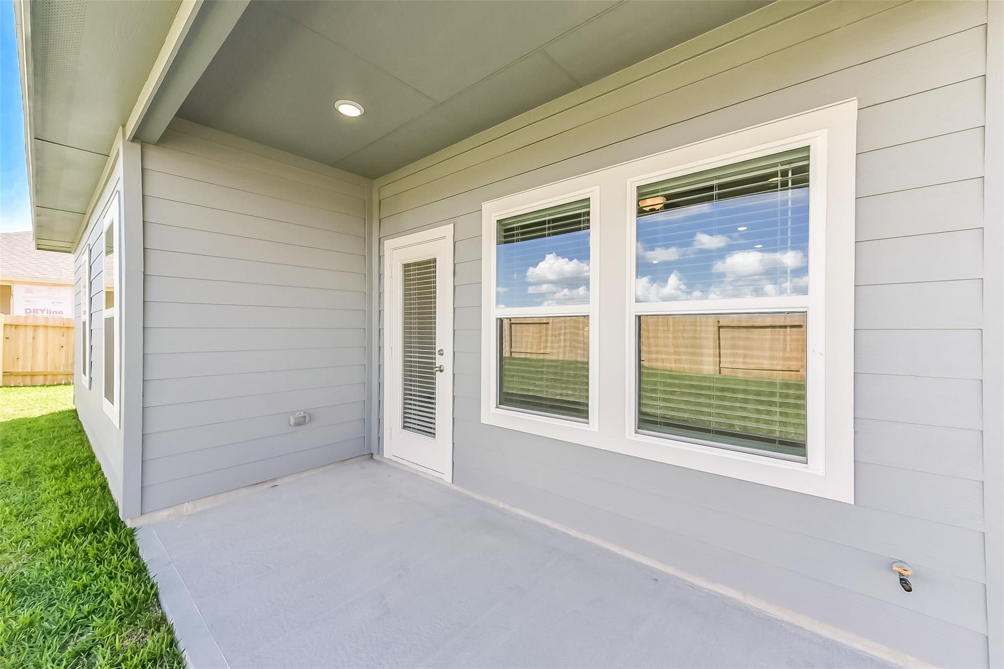 Covered back patio with French doors and large windows on gray-sided exterior of The Costa C 3-car garage home in River Ranch Meadows, Dayton, Texas