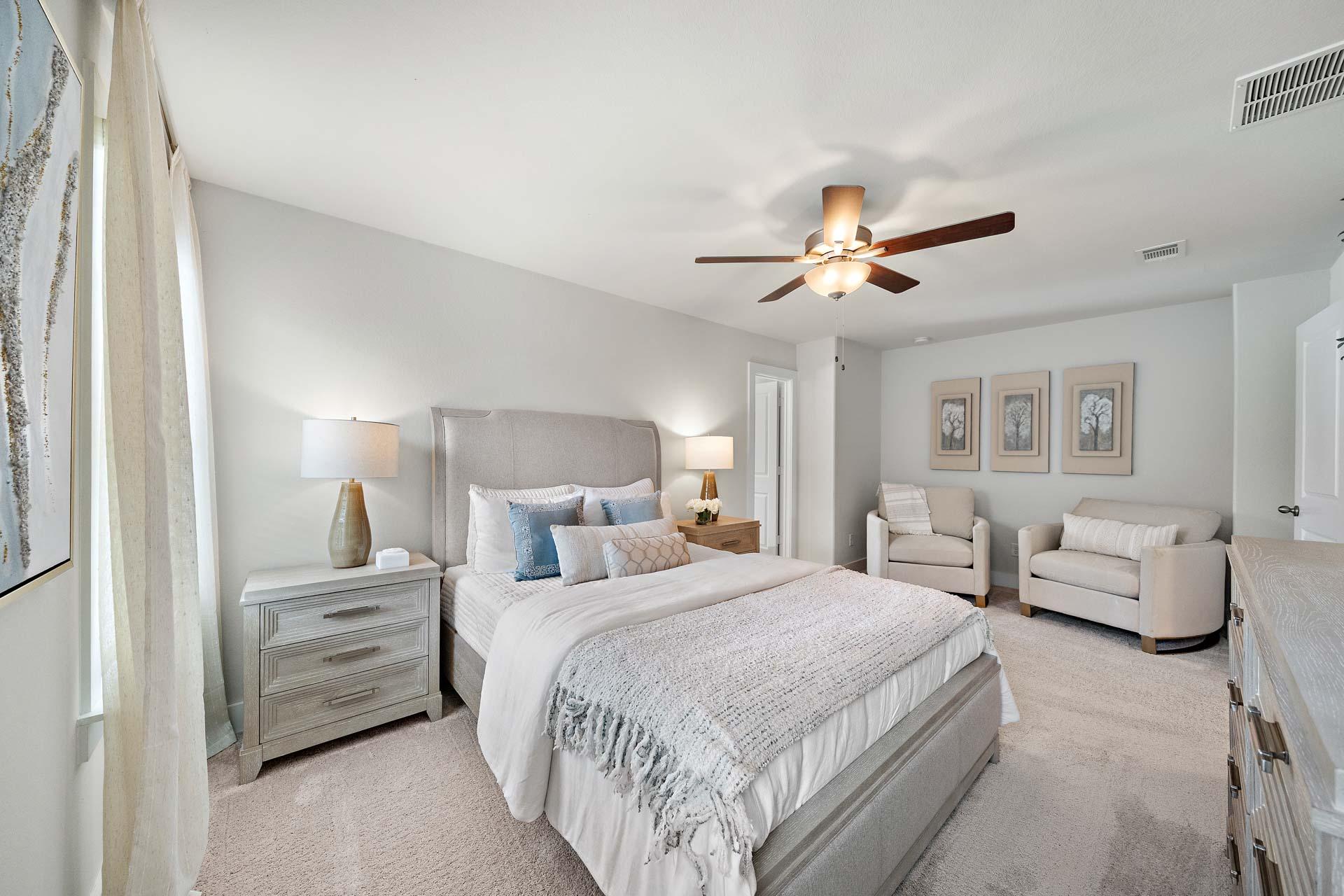Serene primary bedroom at Haven at Kieth Harrow in Cypress TX with upholstered king bed, ceiling fan, and accent chairs