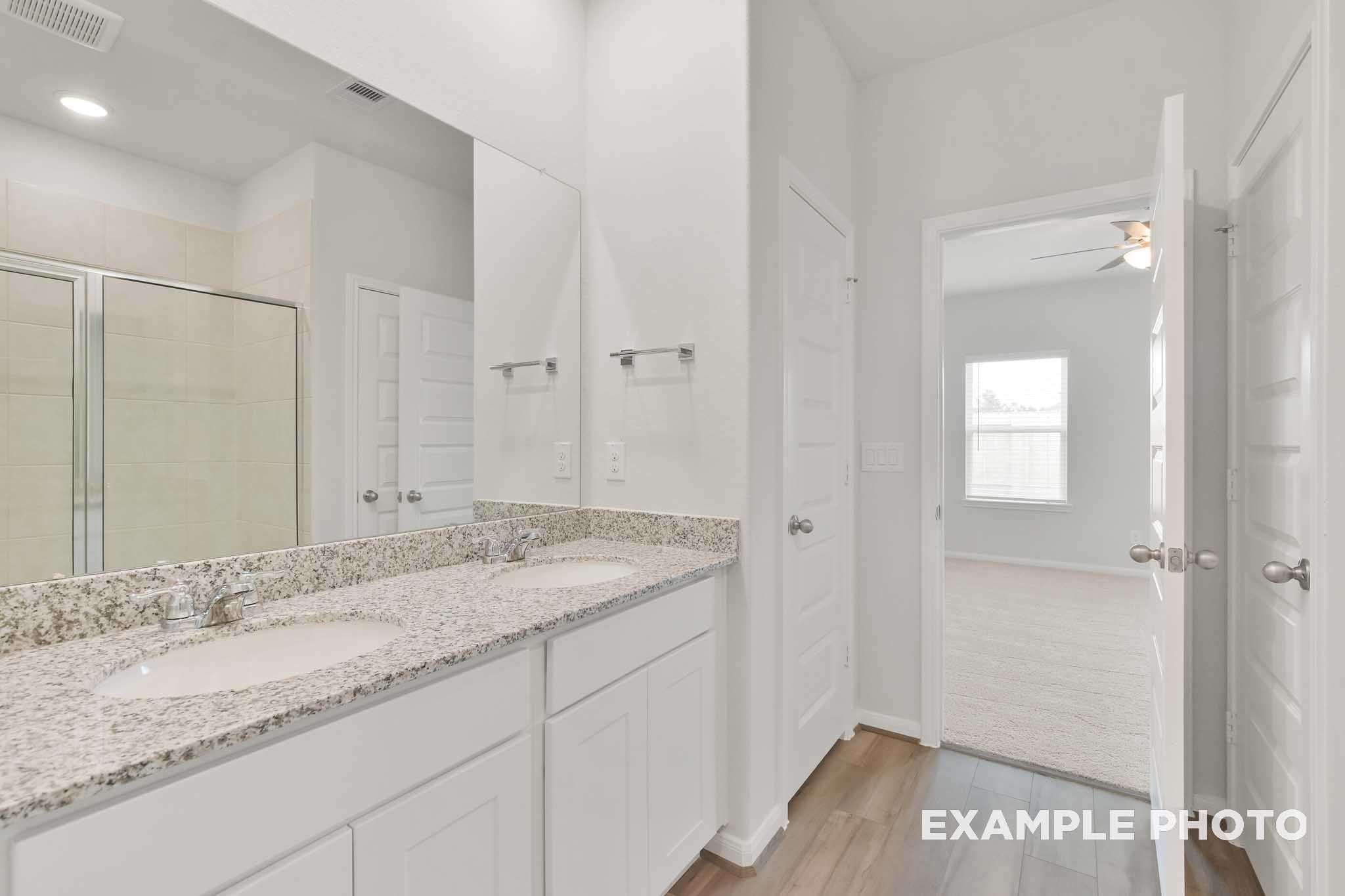 Dual vanity bathroom with granite countertops in The Brazos by Davidson Homes, featuring white cabinetry and tile flooring.