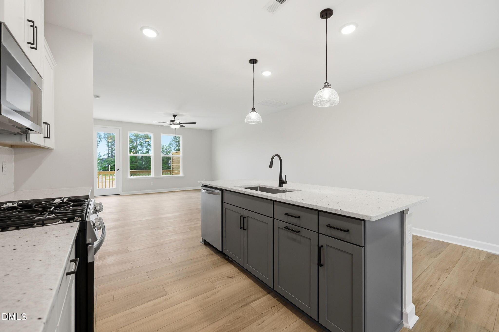 Open-concept kitchen with gray island, granite countertops, and pendant lighting in The Mitchell at Camden Park, Knightdale.