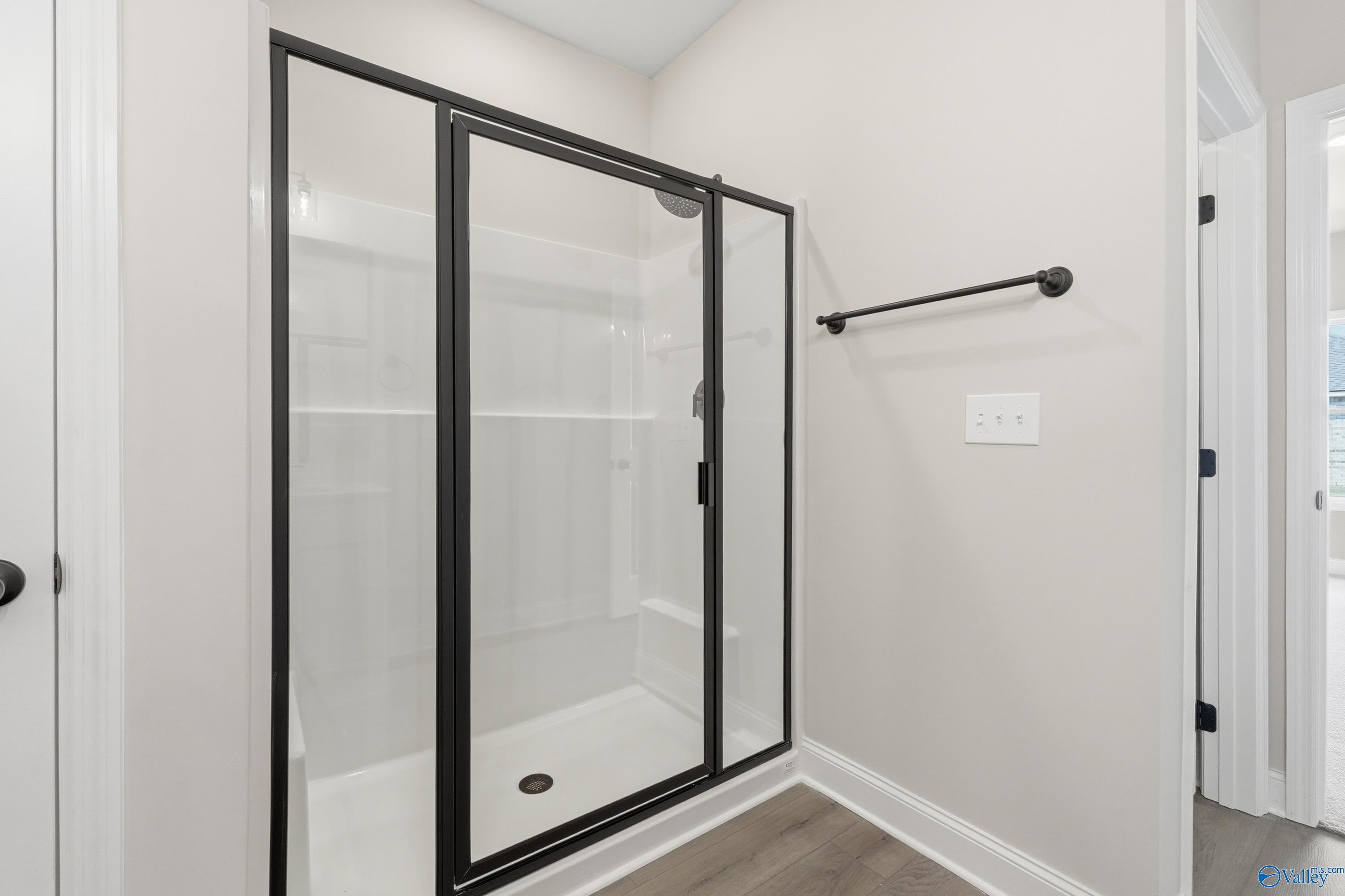 Modern walk-in shower with black-framed glass doors, rainfall head, and white tiles in master bath of Davidson Homes The Franklin C, Meridianville, Alabama