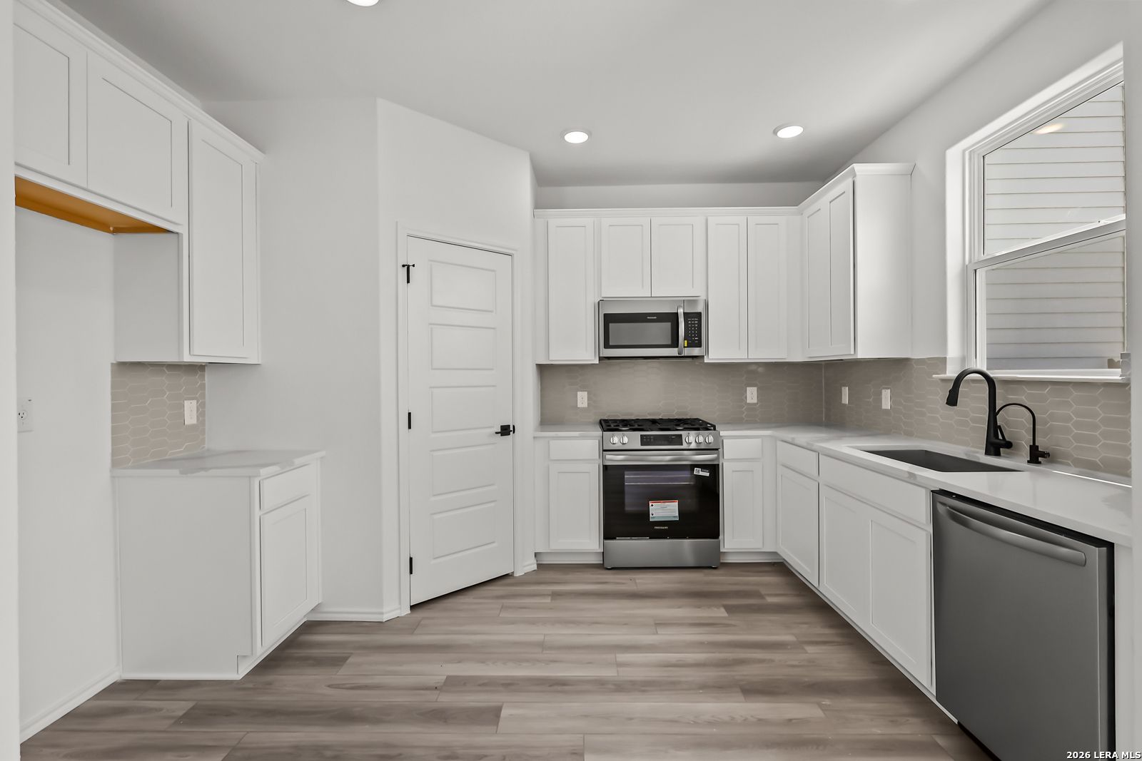 Modern white kitchen with stainless steel appliances and wood-look flooring in The Florence B home, Meadows at Oak Creek.