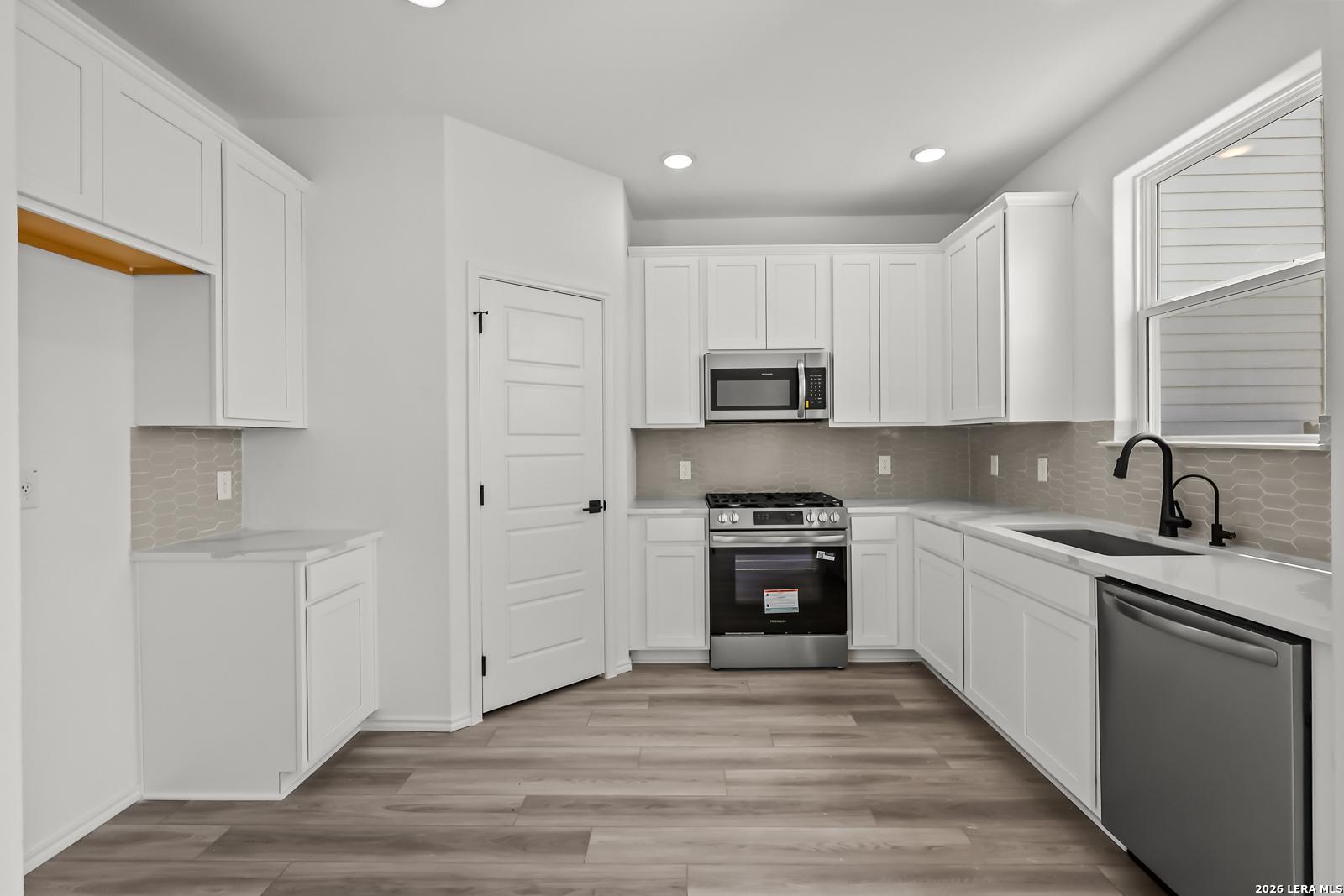 Modern white kitchen with stainless steel appliances and wood-look flooring in The Florence B home, Meadows at Oak Creek.