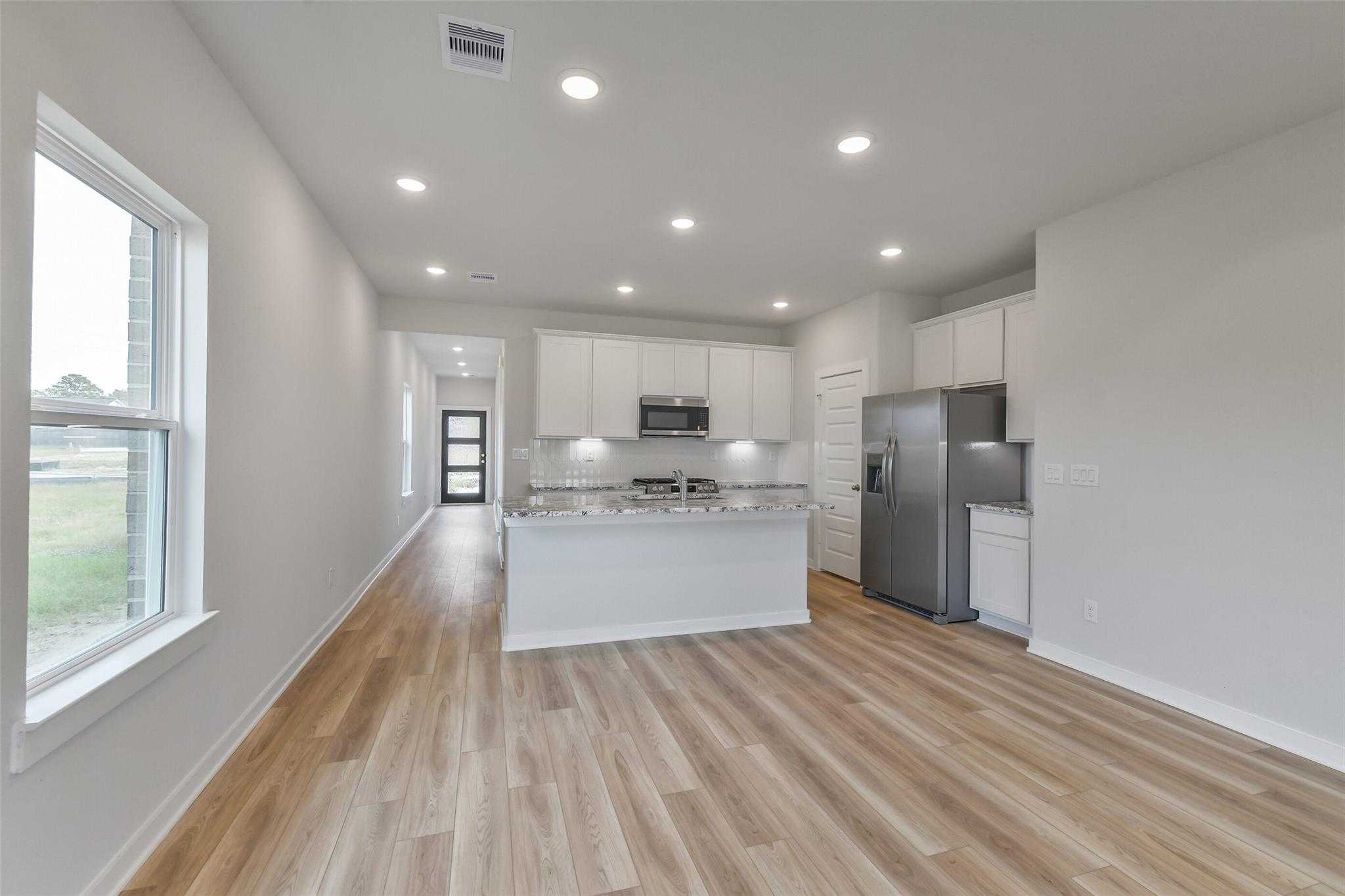 Modern open-concept kitchen with white cabinets, stainless steel appliances, and hardwood floors in Davidson Homes The Colorado G, Magnolia, Texas