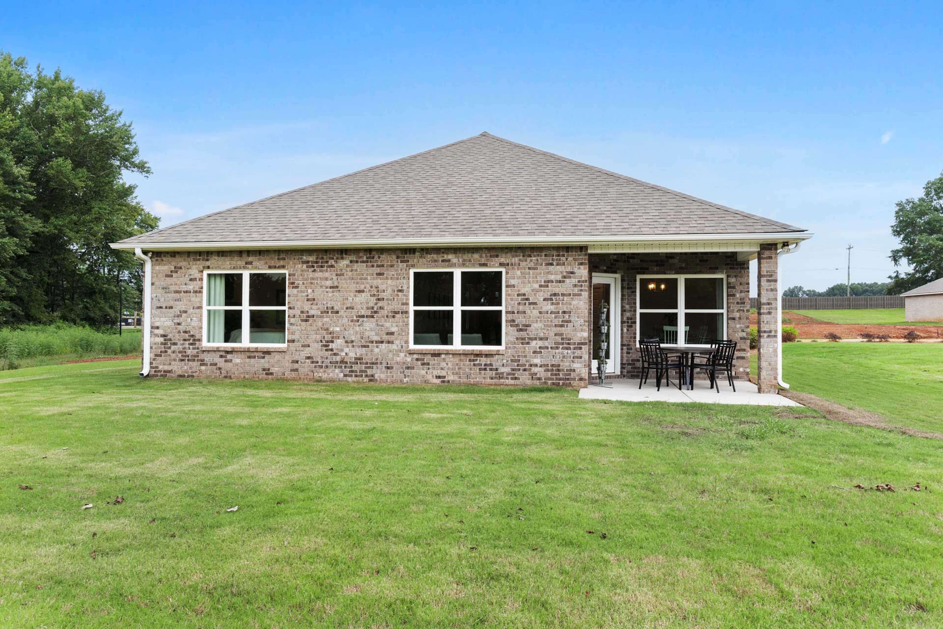 Single-story brick home exterior with covered patio, seating, and lush green lawn at The Meadows in Athens, Alabama