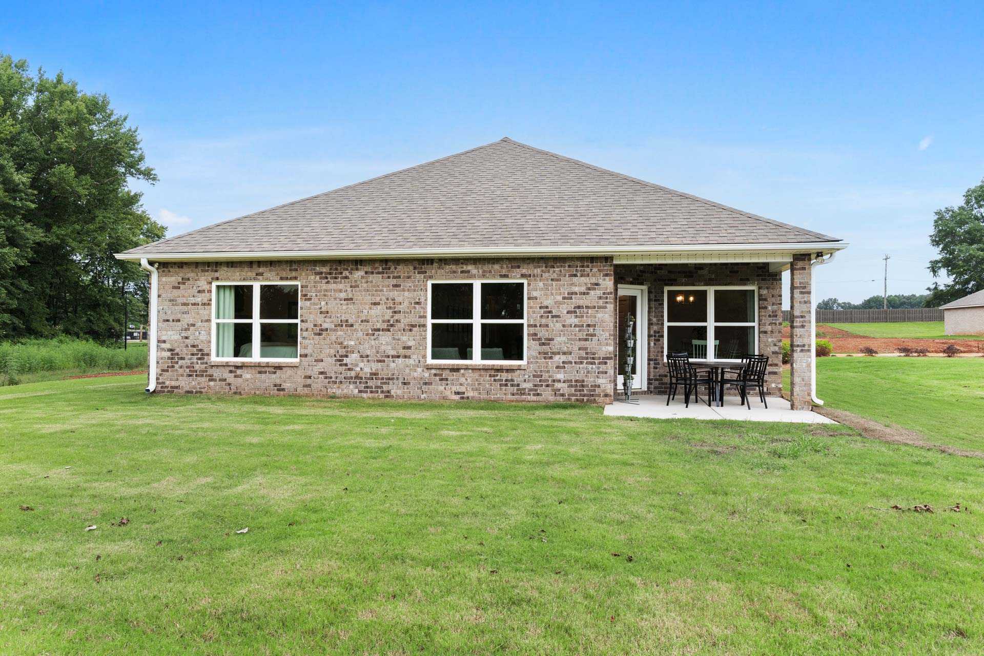 Single-story brick home exterior with covered patio, seating, and lush green lawn at The Meadows in Athens, Alabama