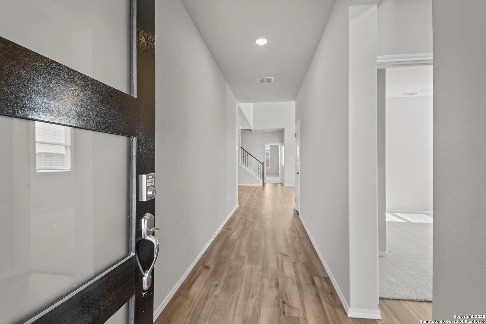 Welcoming entryway with open black glass door to long hallway, light hardwood floors, white walls in The Collin B, Seguin, Texas