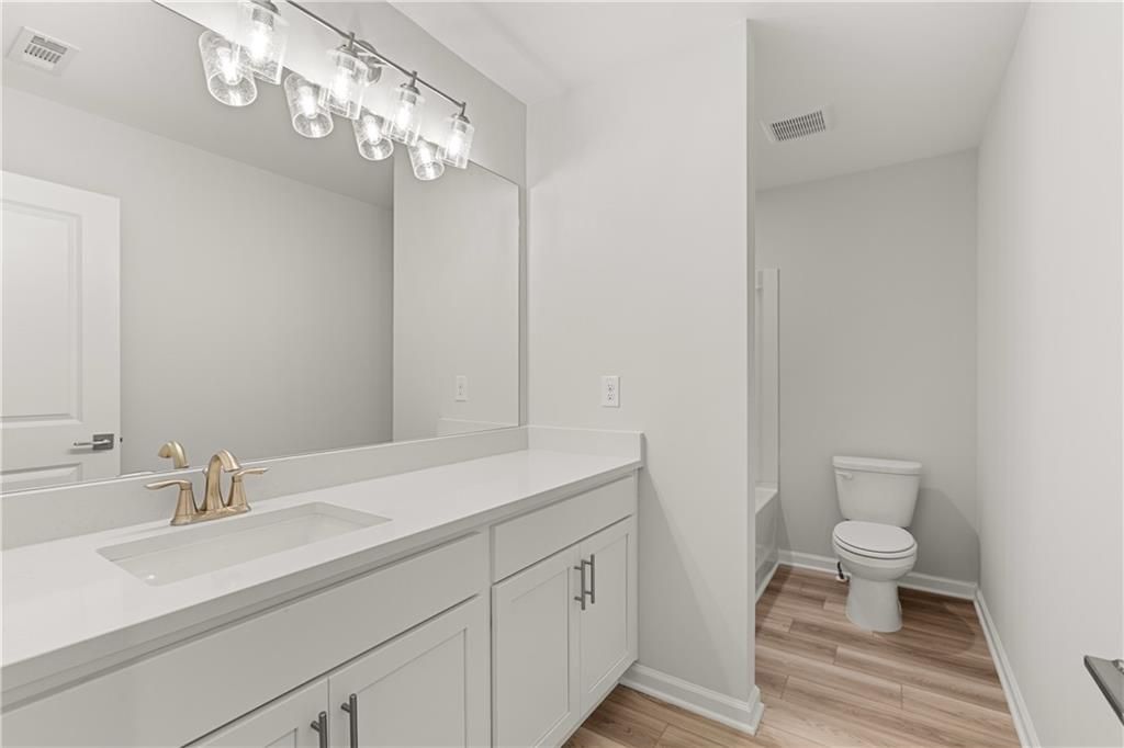 Modern bathroom with white vanity, quartz countertop, and wood-style flooring in The Russell A floor plan, Cedar Farms.