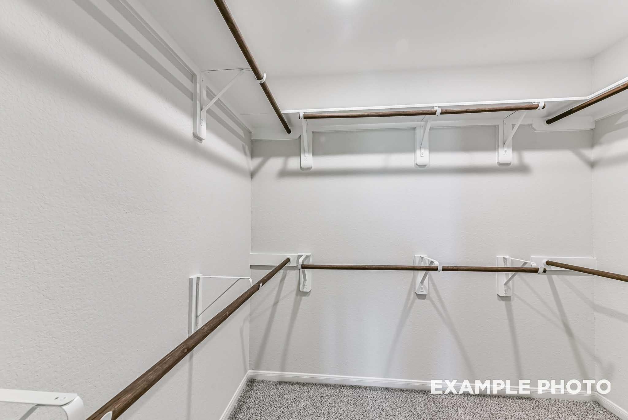 Walk-in closet with tiered wooden hanging rods in The Laguna C floor plan by Davidson Homes in Sunterra, Katy, Texas.
