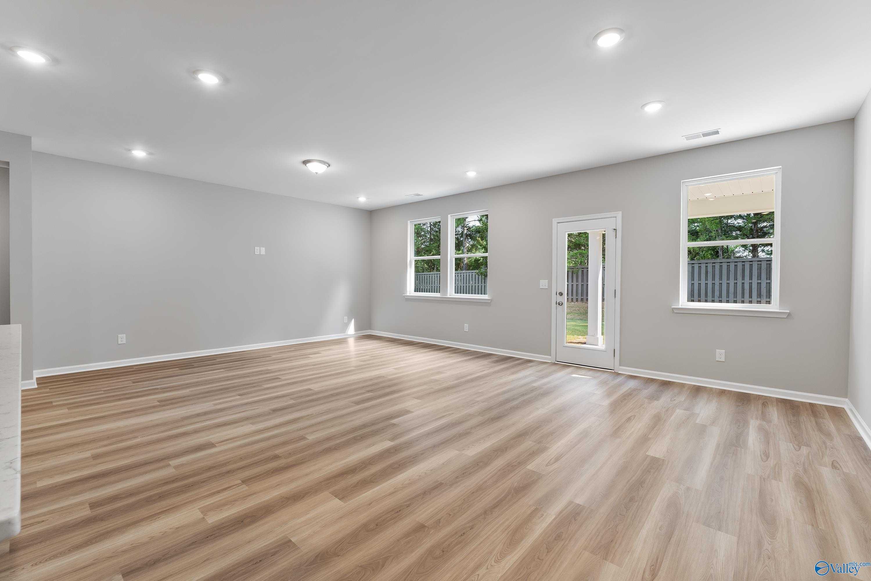 Spacious living room with light wood floors, large windows, and glass door to fenced backyard in The Grace floor plan, Madison, AL