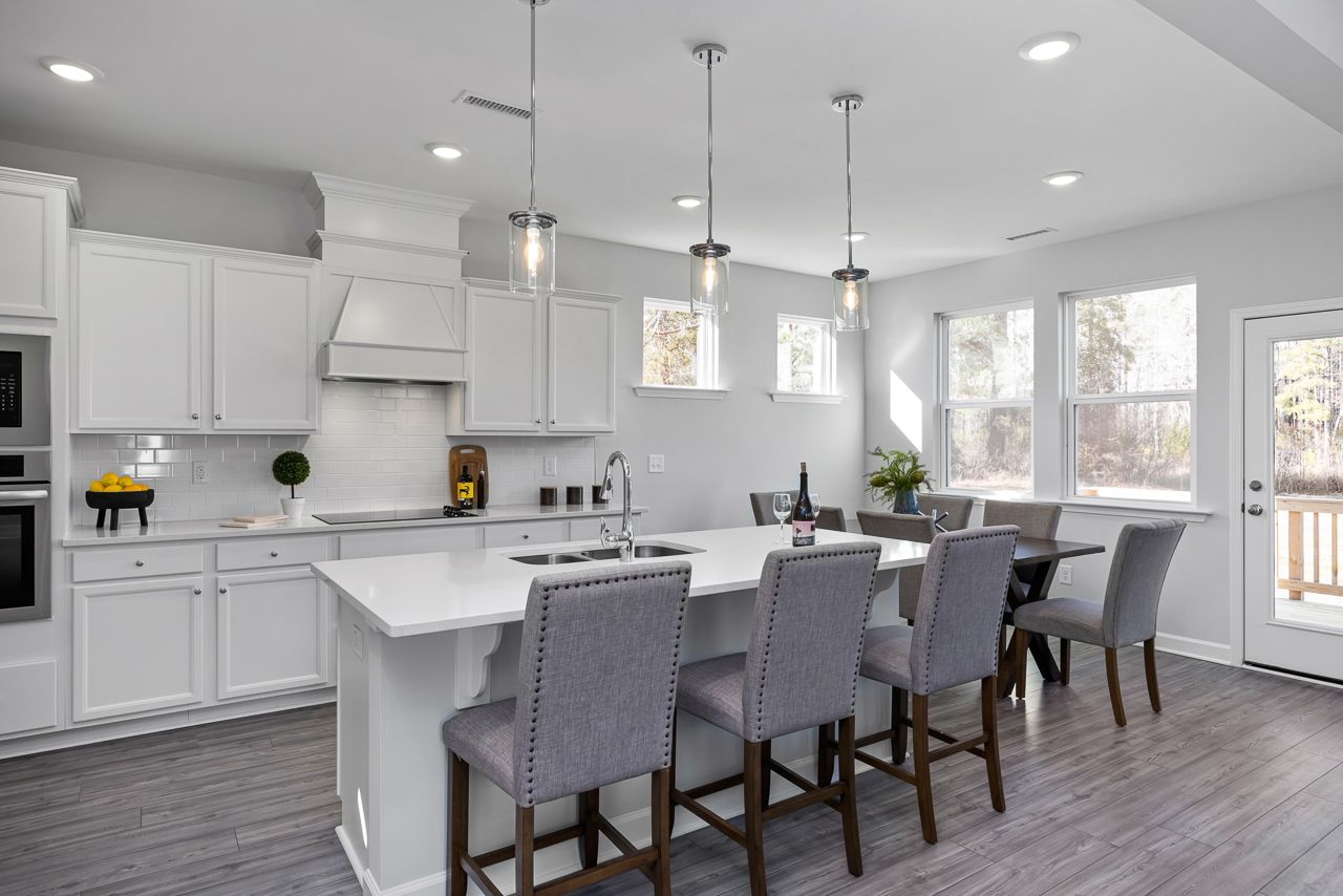Spacious white kitchen in Glenmere Knightdale NC with island sink, pendant lights, bar stools, and adjacent dining area