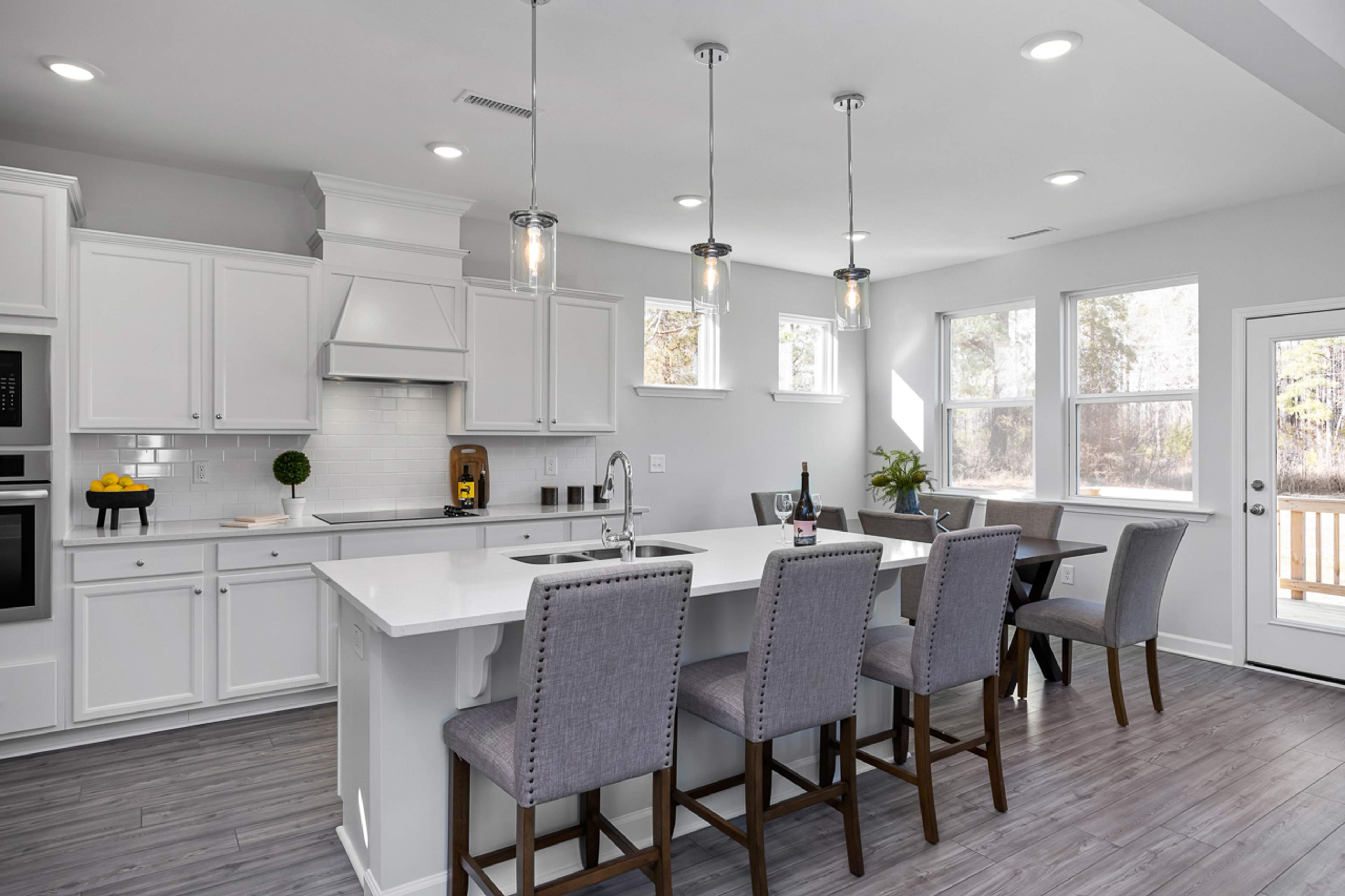 Spacious white kitchen in Glenmere Knightdale NC with island sink, pendant lights, bar stools, and adjacent dining area