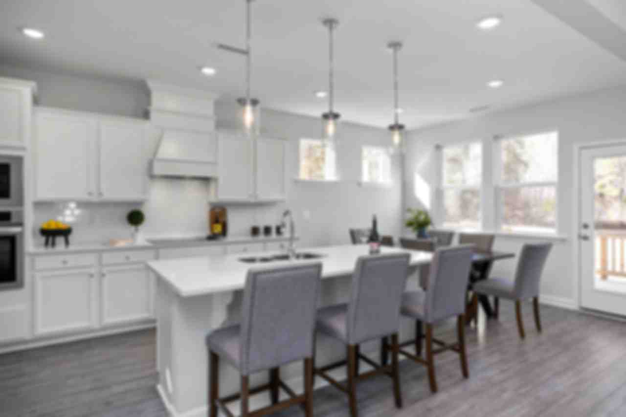 Spacious white kitchen in Glenmere Knightdale NC with island sink, pendant lights, bar stools, and adjacent dining area