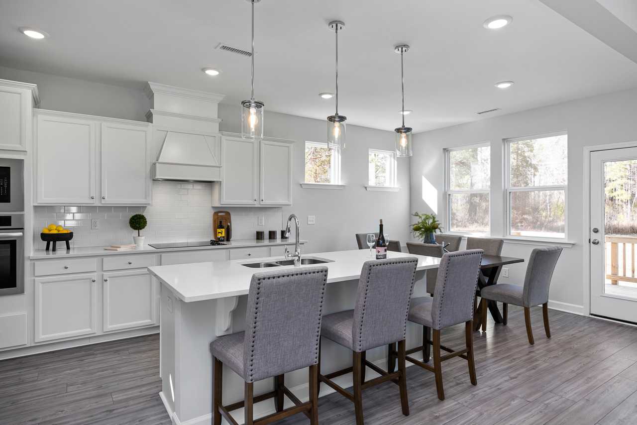 Spacious white kitchen in Glenmere Knightdale NC with island sink, pendant lights, bar stools, and adjacent dining area