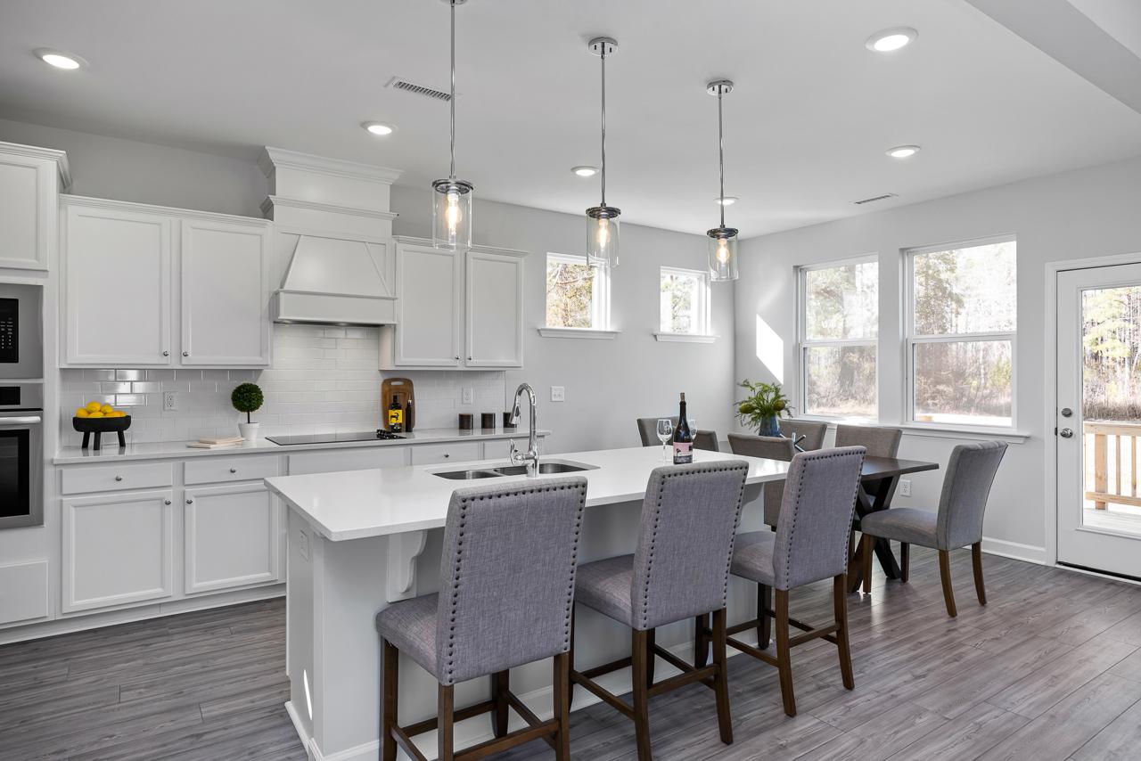 Spacious white kitchen in Glenmere Knightdale NC with island sink, pendant lights, bar stools, and adjacent dining area