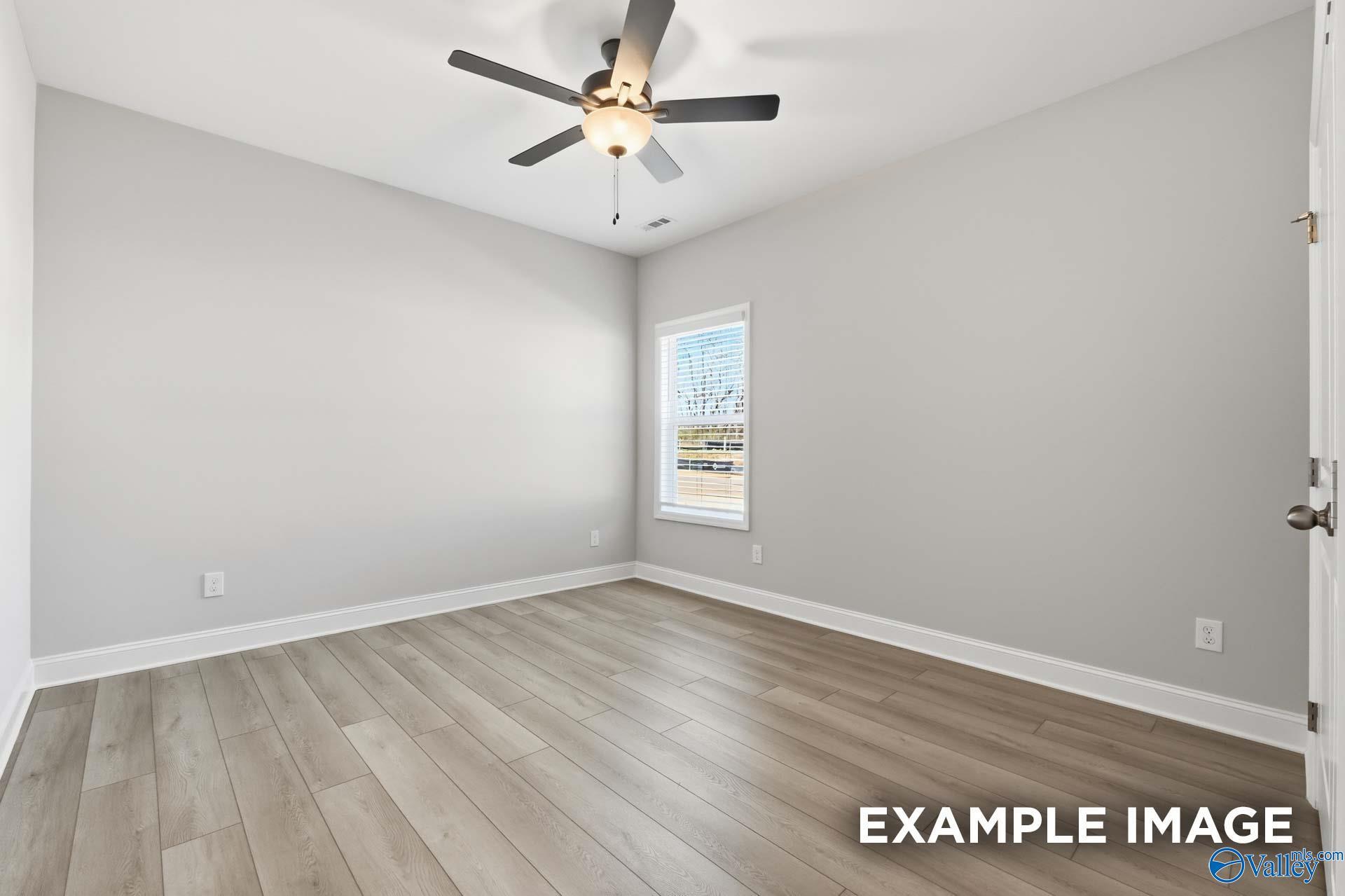 Empty bedroom with light gray walls, ceiling fan, blinds-covered window, and luxury vinyl plank flooring in Davidson Homes The Harrison C, Madison, Alabama