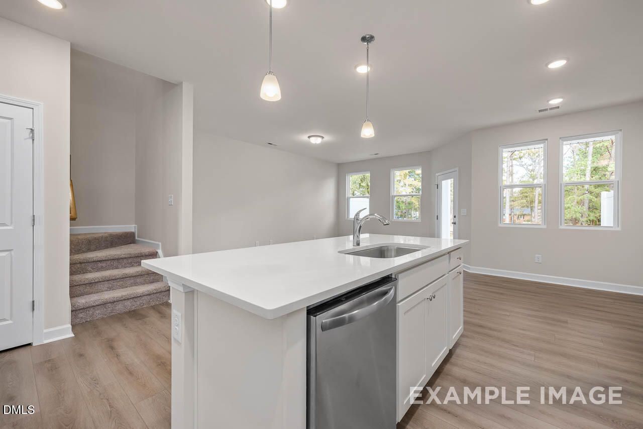Modern open-concept kitchen with white quartz island, stainless dishwasher, hardwood floors, and large windows in Davidson Homes The Graham, Fuquay-Varina, NC