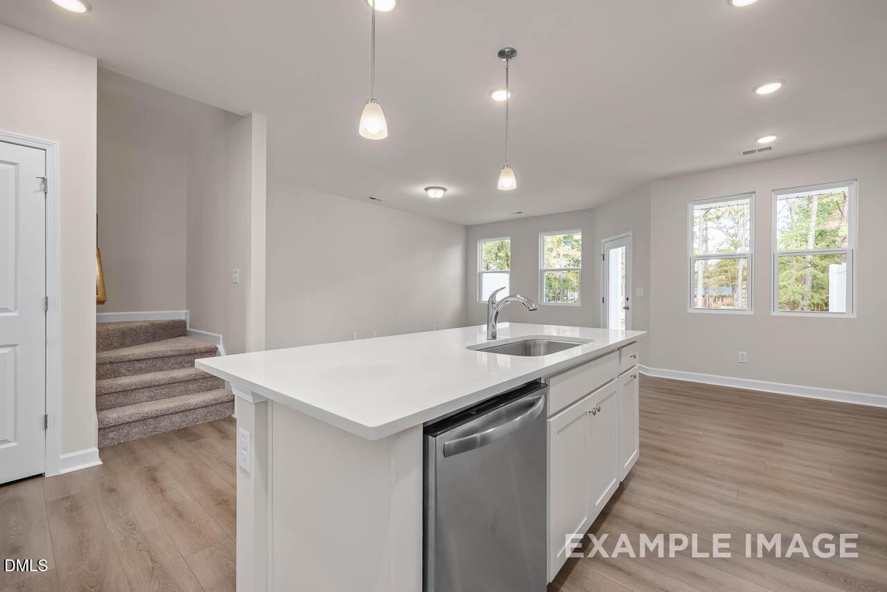 Modern open-concept kitchen with white quartz island, stainless dishwasher, hardwood floors, and large windows in Davidson Homes The Graham, Fuquay-Varina, NC