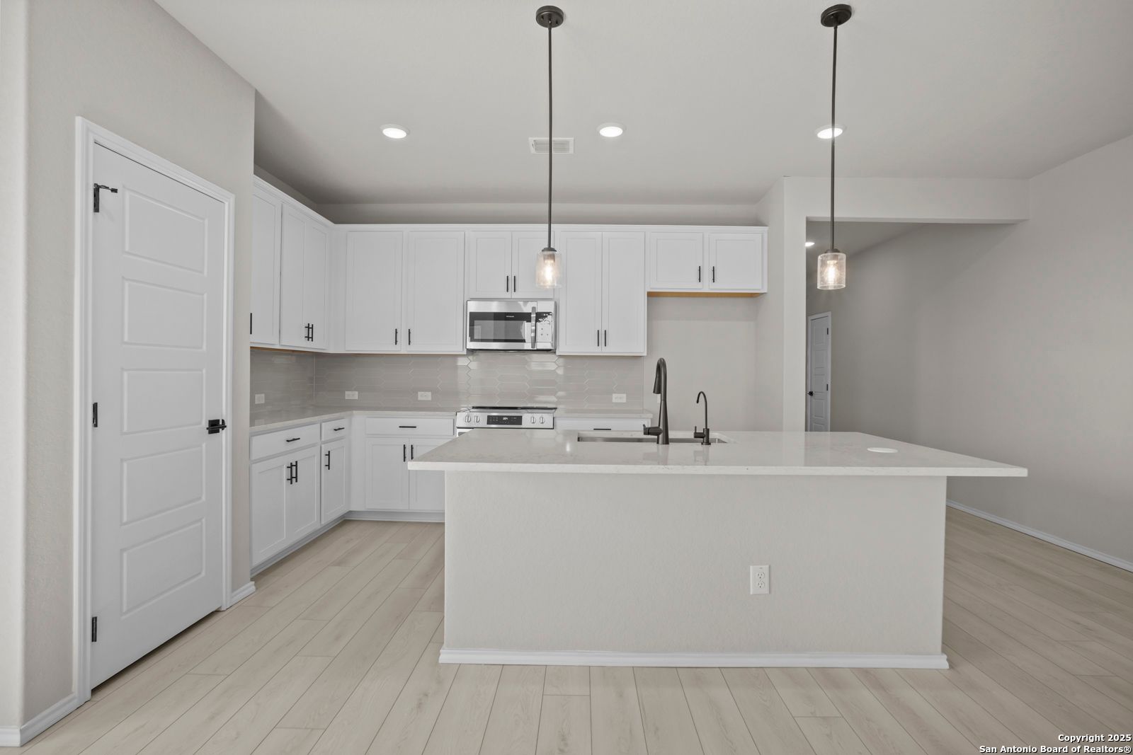 Modern white kitchen island with stainless appliances and pendant lights in Davidson Homes The Daphne H, Seguin, Texas