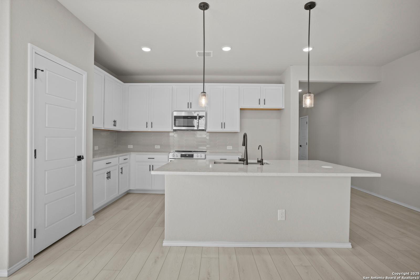Modern white kitchen island with stainless appliances and pendant lights in Davidson Homes The Daphne H, Seguin, Texas