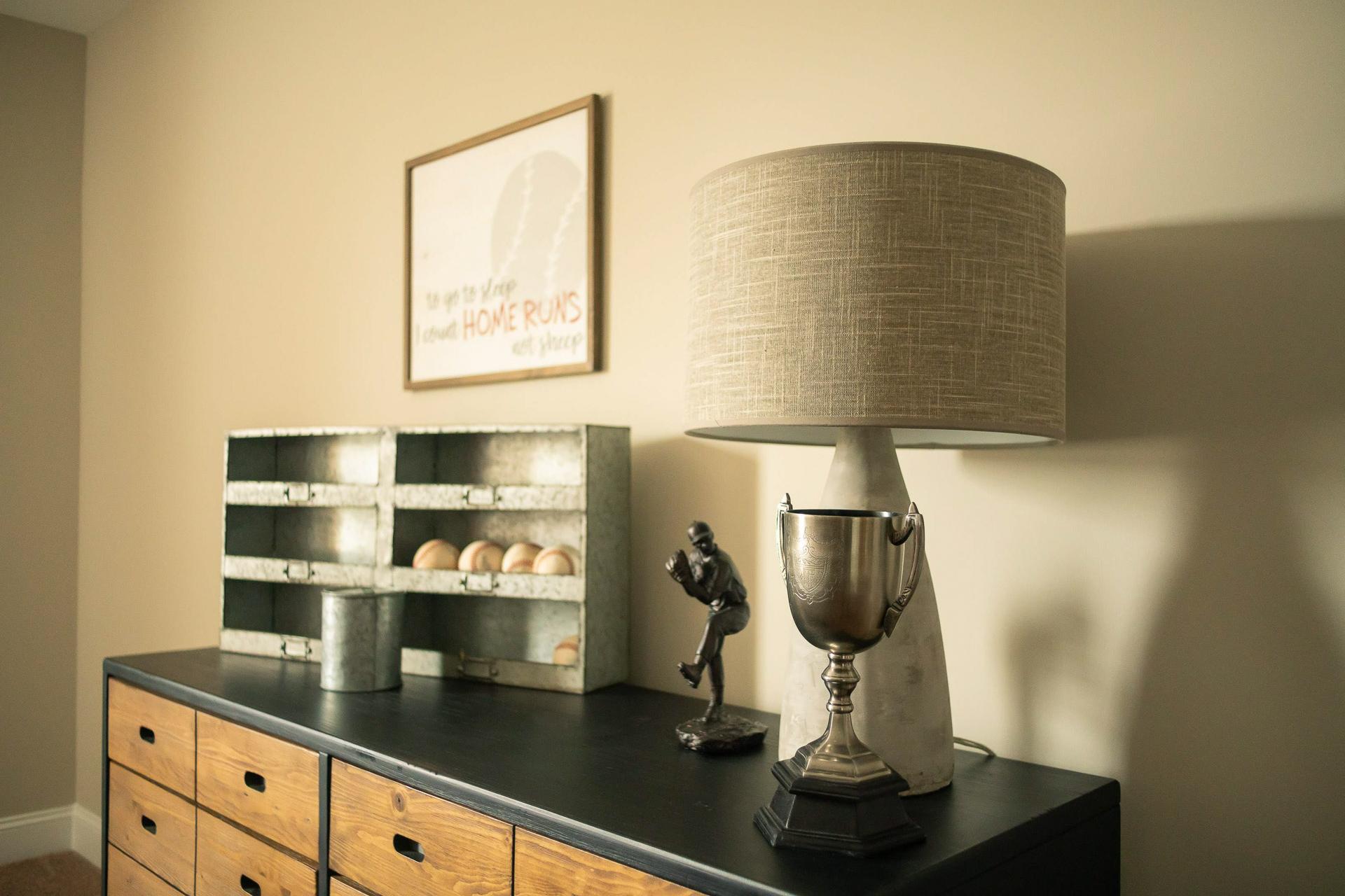 Rustic wooden dresser with galvanized bin of eggs, baseball trophy, figurine, and linen lamp in Summer Pointe Madison AL home