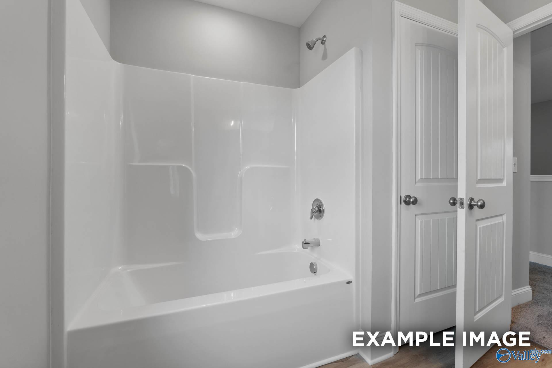 Modern bathroom with white bathtub, glass shower enclosure, and light gray walls in Davidson Homes The Shelby B, New Market, Alabama