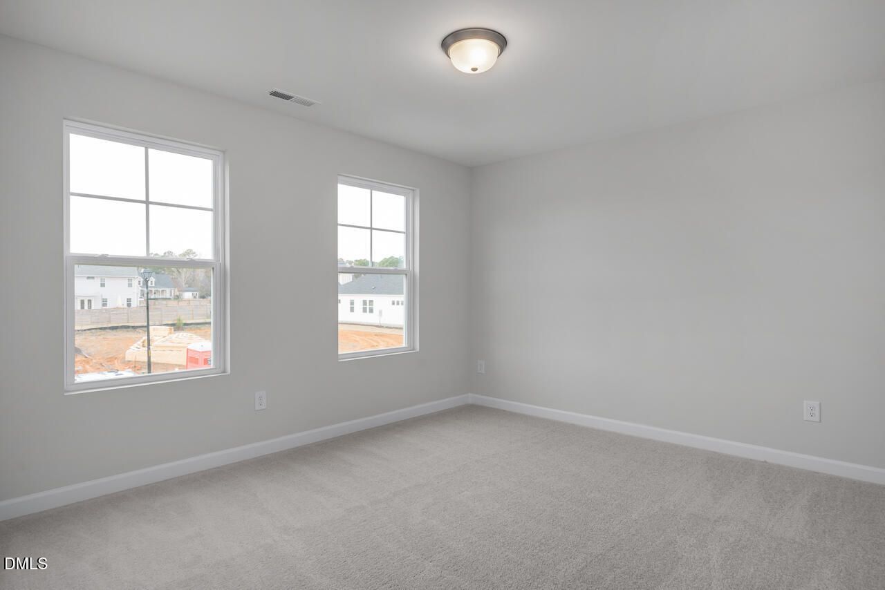 Spacious empty bedroom with large windows, gray carpet, and neutral walls in Davidson Homes The Gavin B, Lillington, NC