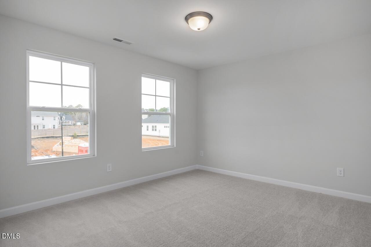 Spacious empty bedroom with large windows, gray carpet, and neutral walls in Davidson Homes The Gavin B, Lillington, NC