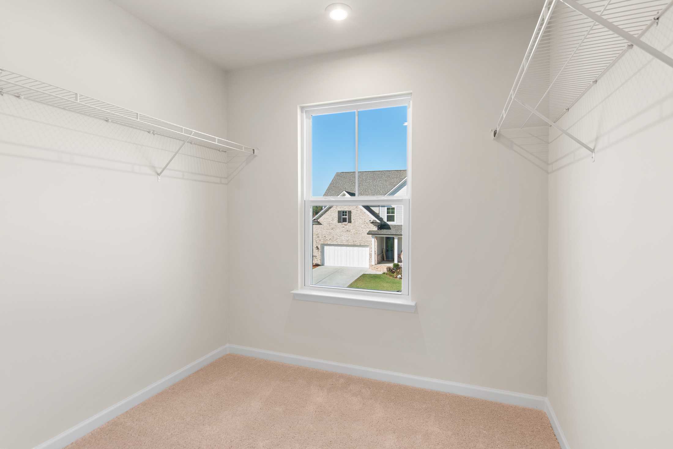 Spacious walk-in closet in The Willow B master suite featuring wire shelving, hanging rods, and window overlooking two-story home exterior