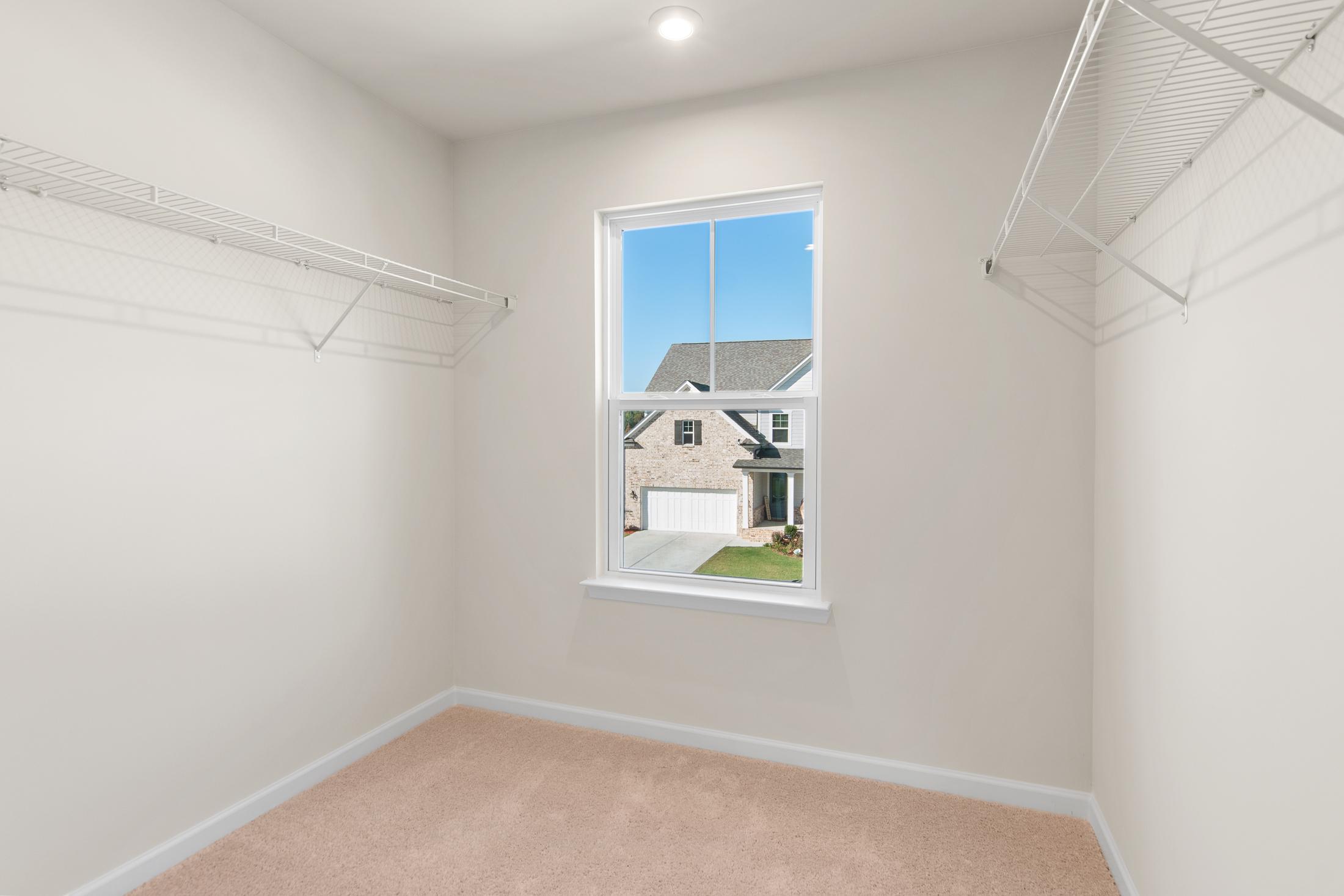 Spacious walk-in closet in The Willow B master suite featuring wire shelving, hanging rods, and window overlooking two-story home exterior