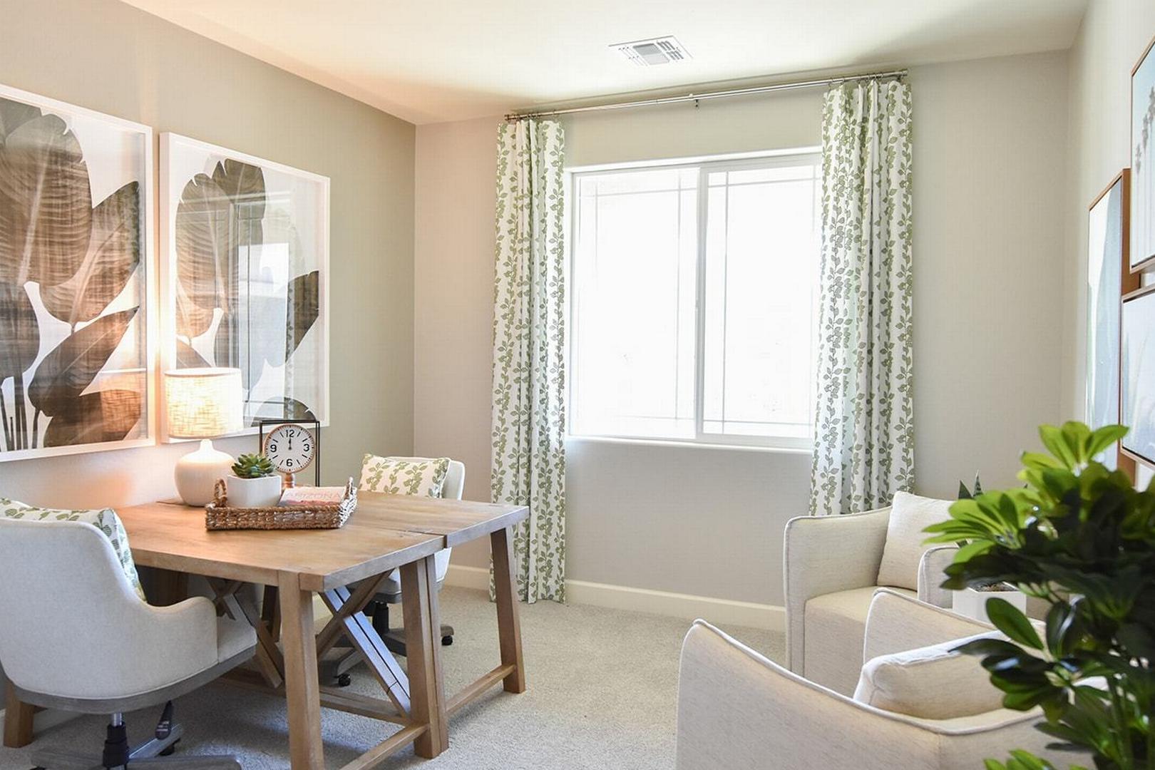 Cozy home office in The Summit E by Evermore Homes featuring wooden desk, botanical wall art, and window with sheer curtains