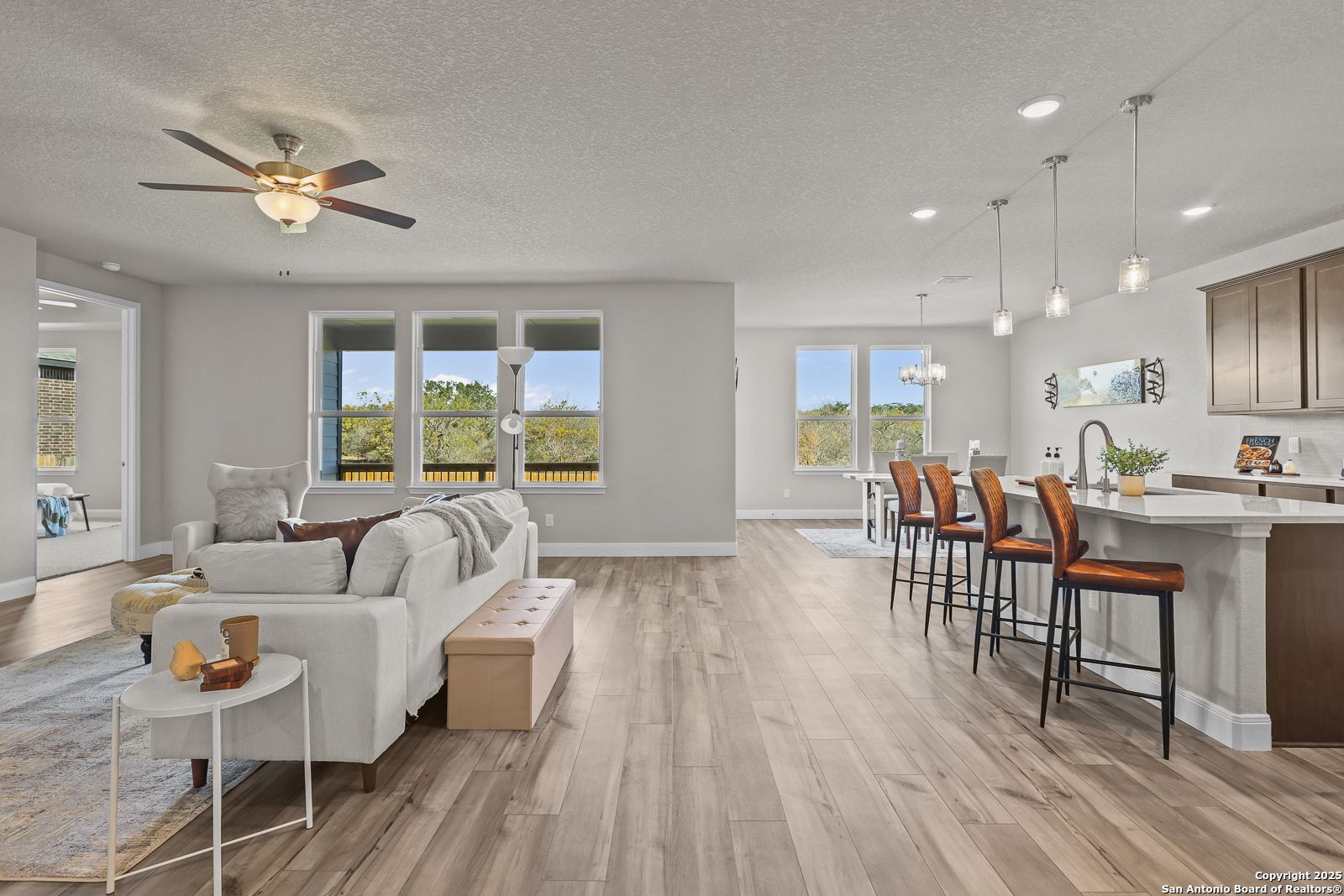 Spacious open-concept living and kitchen with large windows, hardwood floors, island bar stools in Davidson Homes The Jennings G, Castroville TX