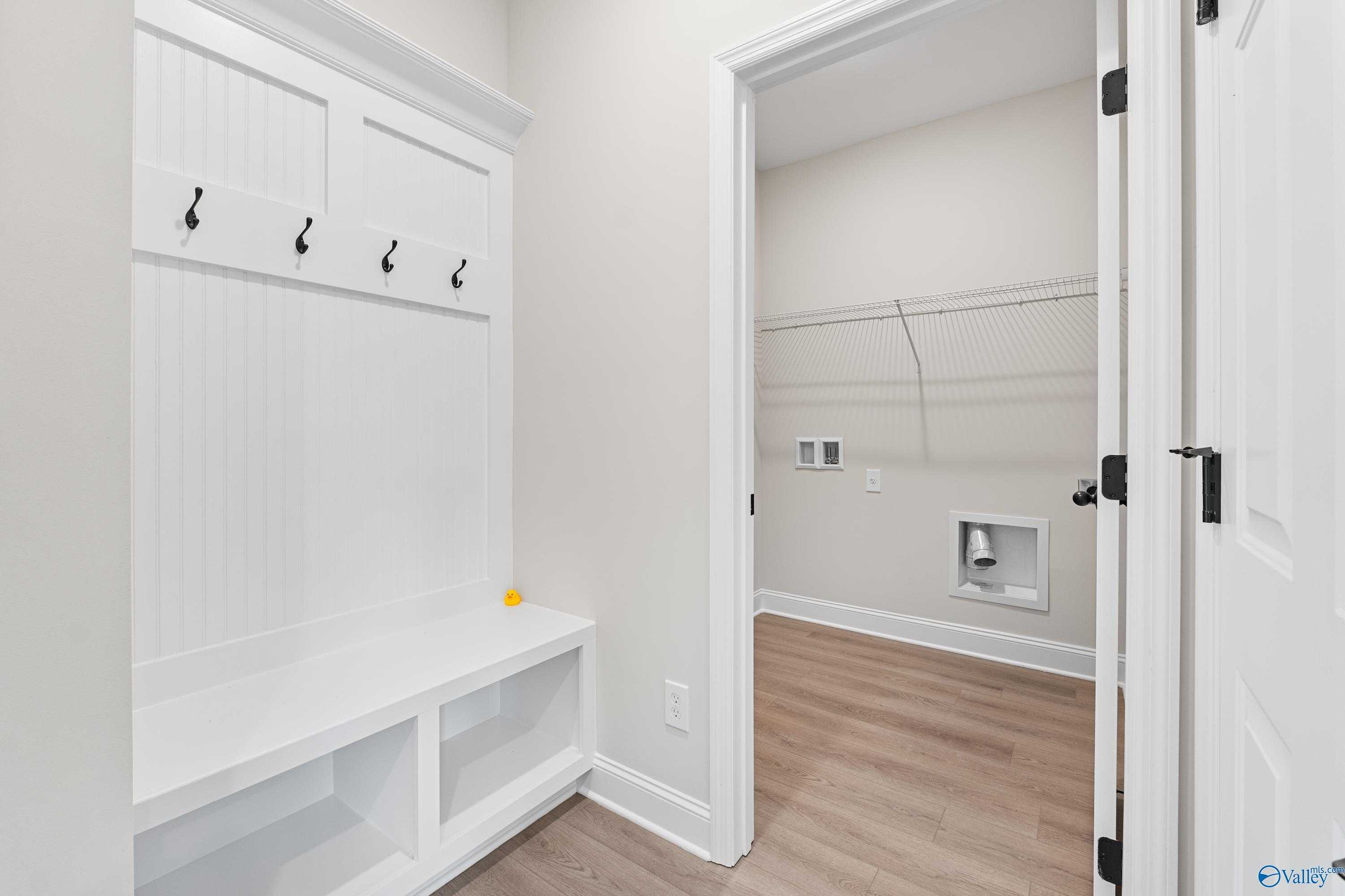 White paneled mudroom with coat hooks, bench, and adjacent laundry room in Davidson Homes The Franklin B, Hazel Green, AL