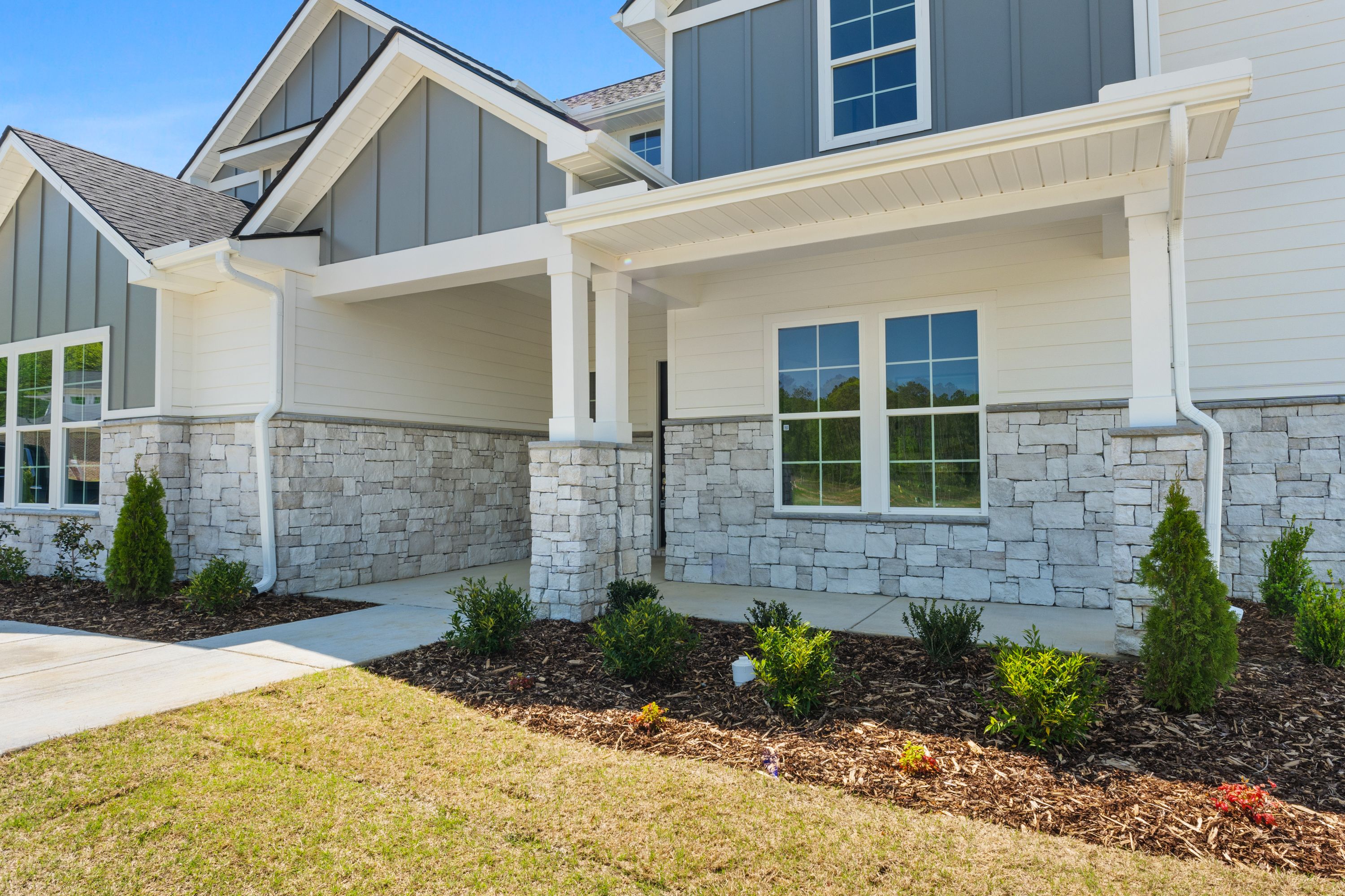 Modern single-story elevation of The Haven D featuring gray siding, stone accents, covered porch, and landscaped yard