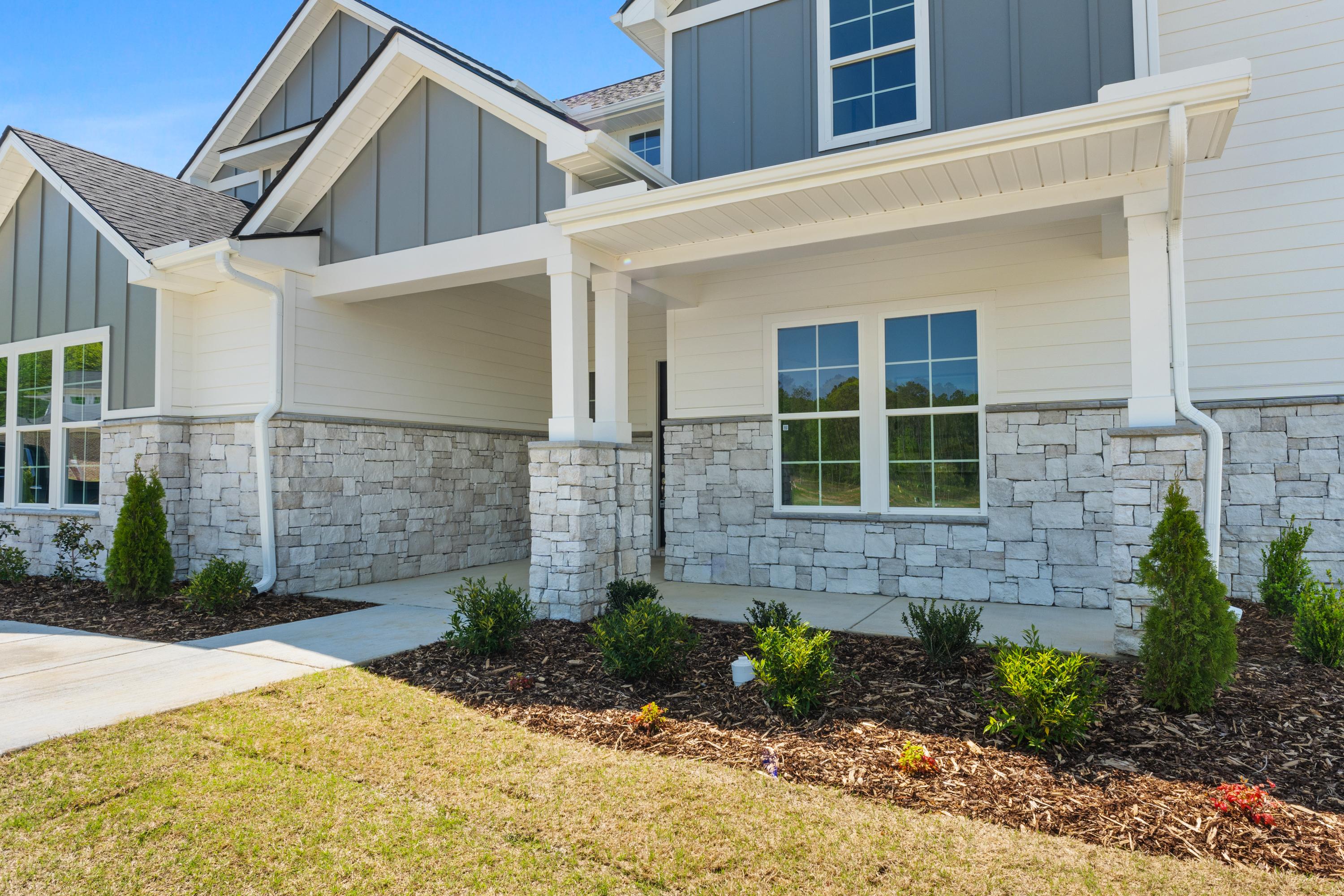 Modern single-story elevation of The Haven D featuring gray siding, stone accents, covered porch, and landscaped yard
