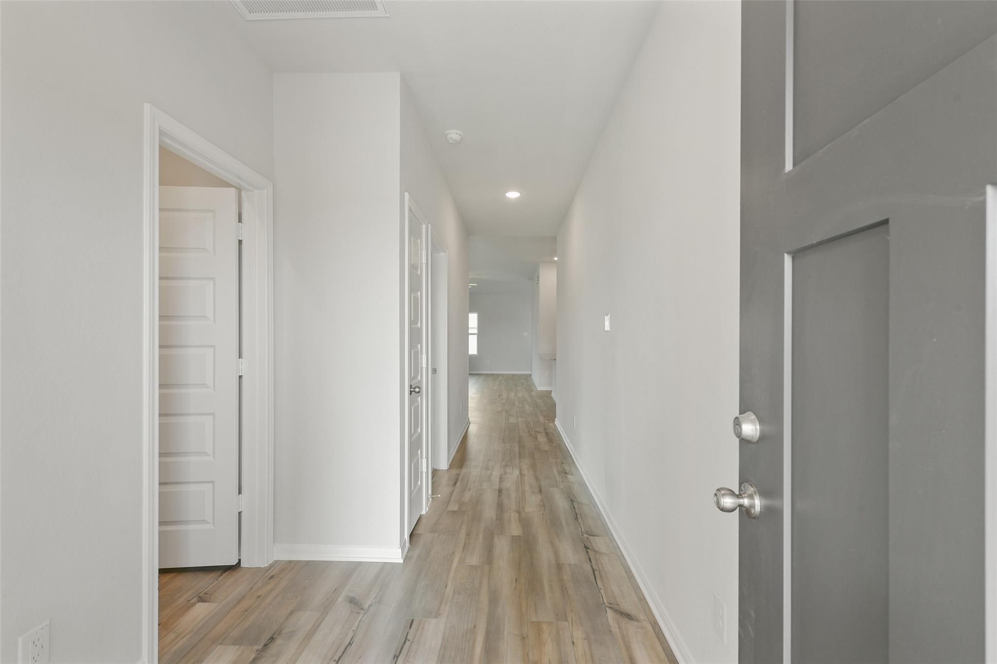 Bright hallway with light oak floors, white walls, and open doors in Davidson Homes The Laguna B, Dayton, Texas