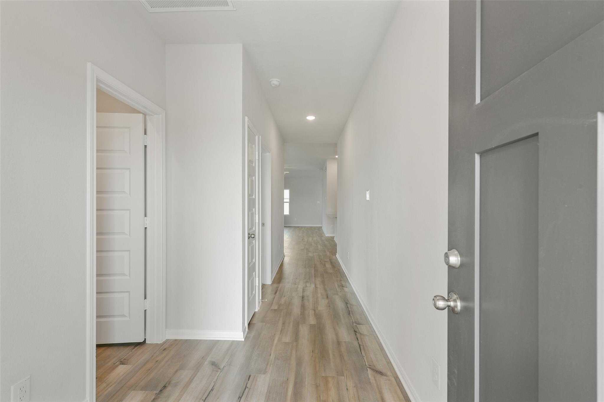 Bright hallway with light oak floors, white walls, and open doors in Davidson Homes The Laguna B, Dayton, Texas