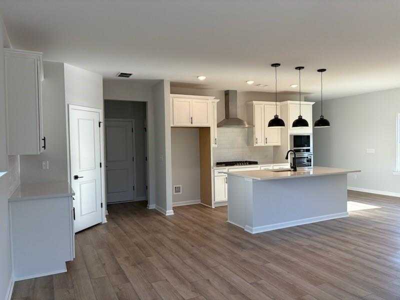 Modern white kitchen with large island, black pendant lights, and open layout in Davidson Homes The Rabun C, Winder, GA