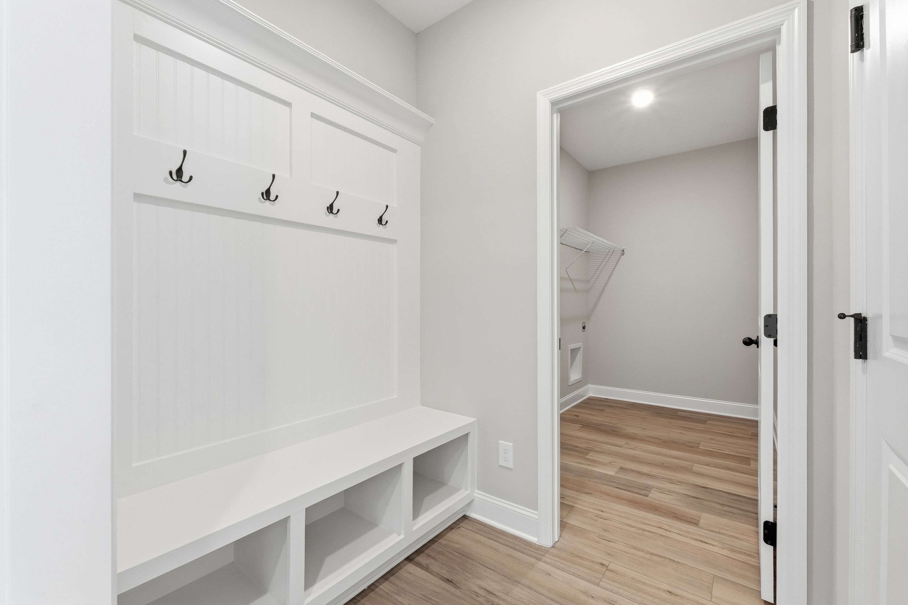Spacious mudroom in The Rockford home with white built-in bench, coat hooks, and laundry room access on hardwood floors