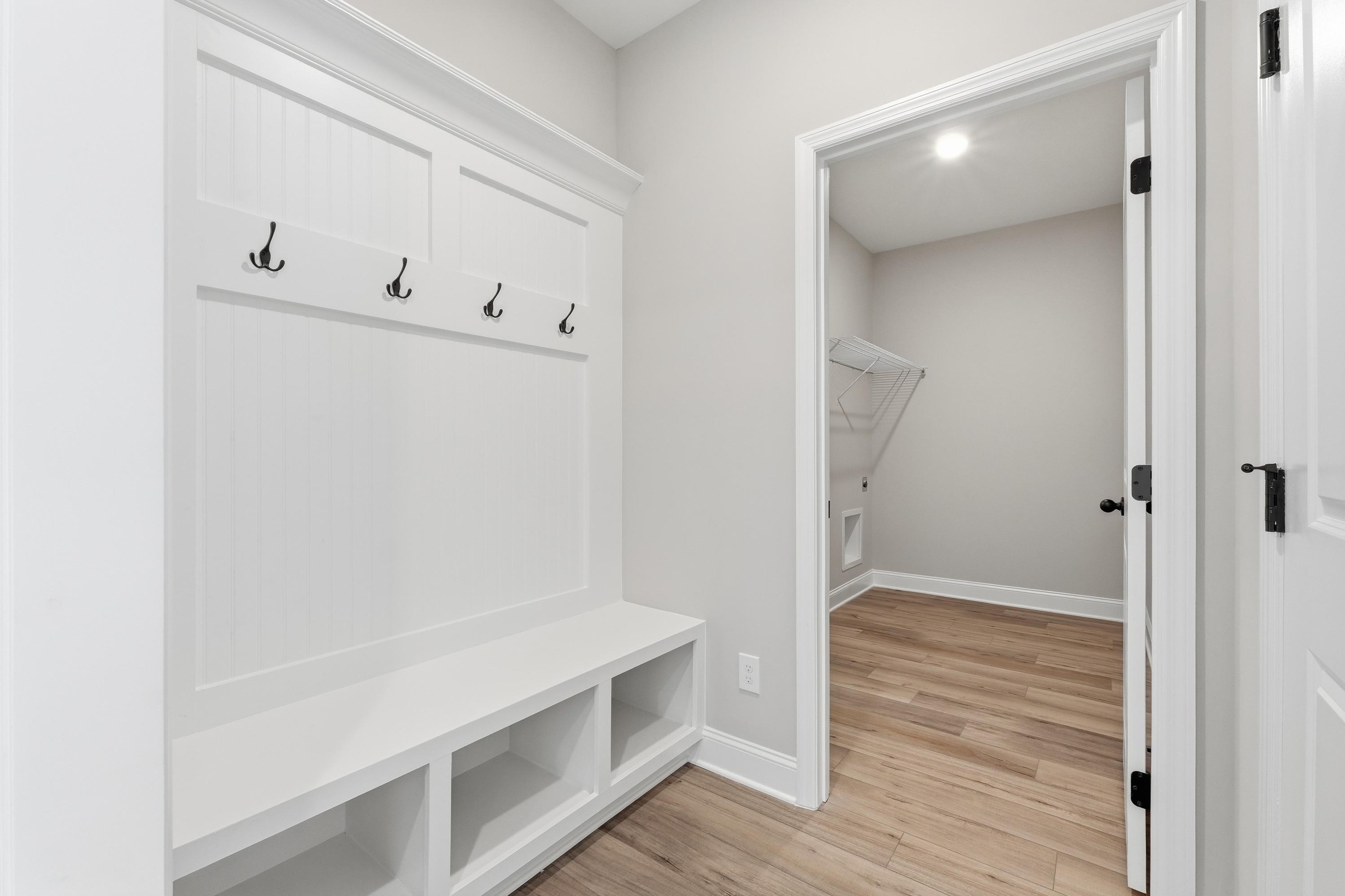 Spacious mudroom in The Rockford home with white built-in bench, coat hooks, and laundry room access on hardwood floors
