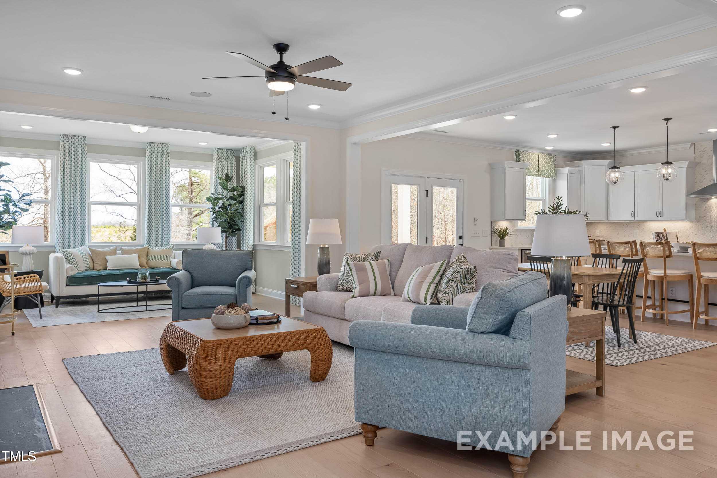 Open-concept living room with blue sofas, rattan coffee table, and large windows in Davidson Homes The Crawford B, Raleigh, NC