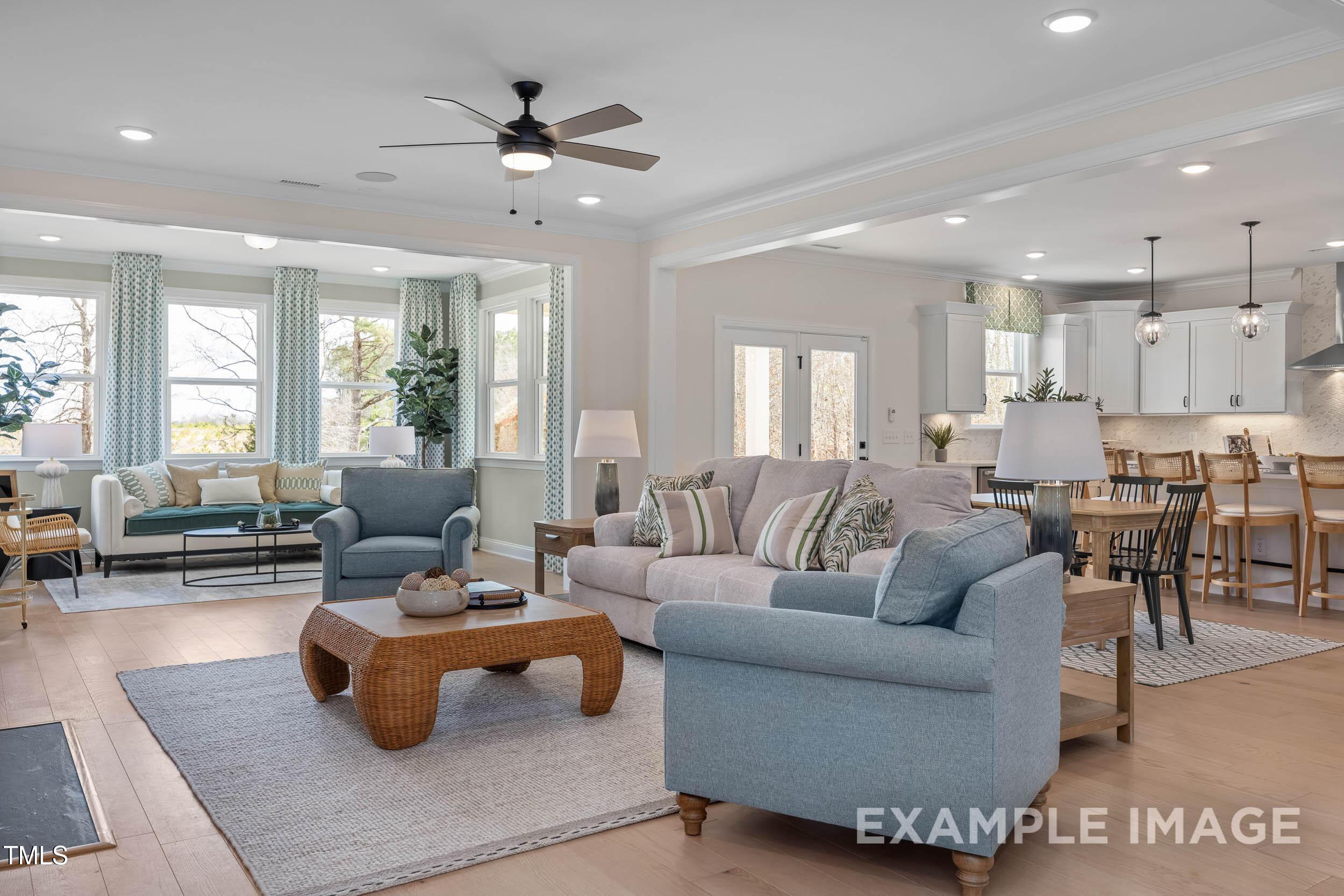 Open-concept living room with blue sofas, rattan coffee table, and large windows in Davidson Homes The Crawford B, Raleigh, NC