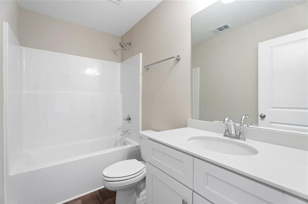 Bright bathroom with white tub-shower combo, single vanity sink, toilet, and wood flooring in Davidson Homes The Washington, Phenix City