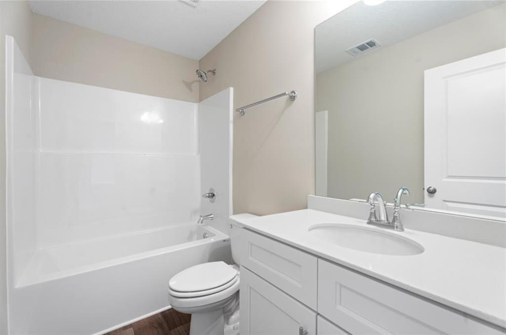 Bright bathroom with white tub-shower combo, single vanity sink, toilet, and wood flooring in Davidson Homes The Washington, Phenix City