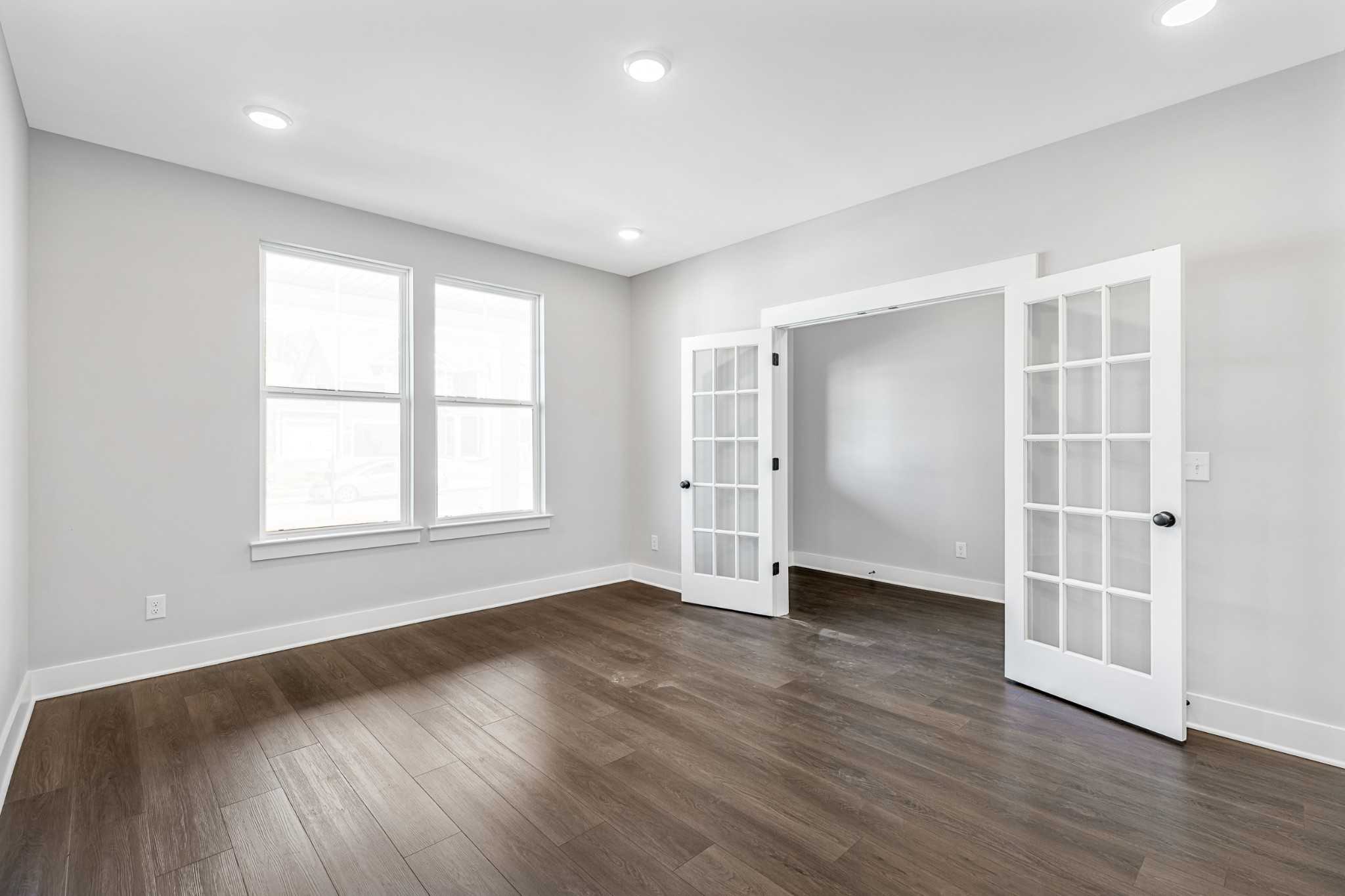 Spacious living room with hardwood floors, open French doors, large windows, and neutral walls in Davidson Homes The Henry C, White House, TN