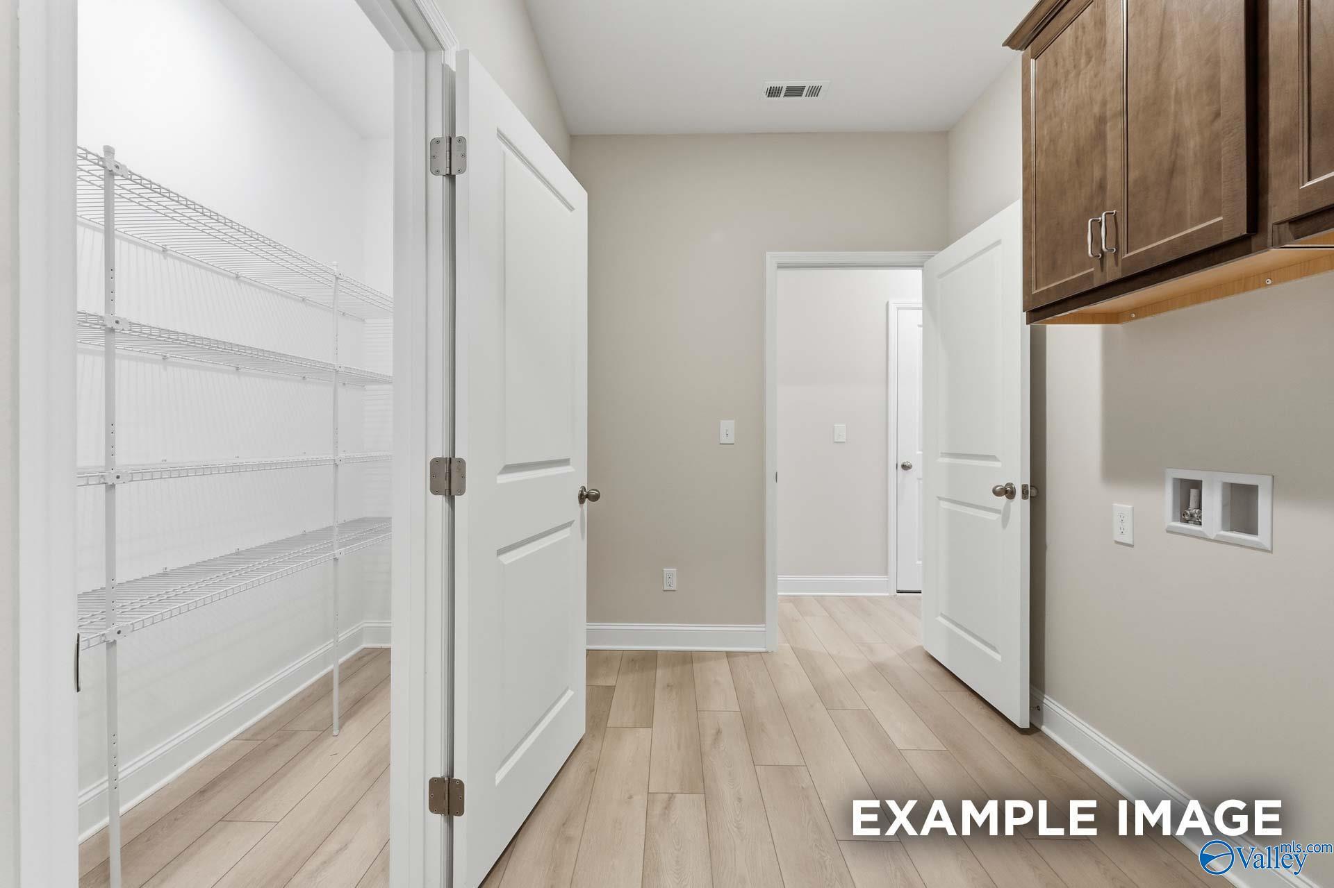 Bright laundry room with wire shelving, wood cabinets, and hardwood floors in The Harrison C, Madison Alabama