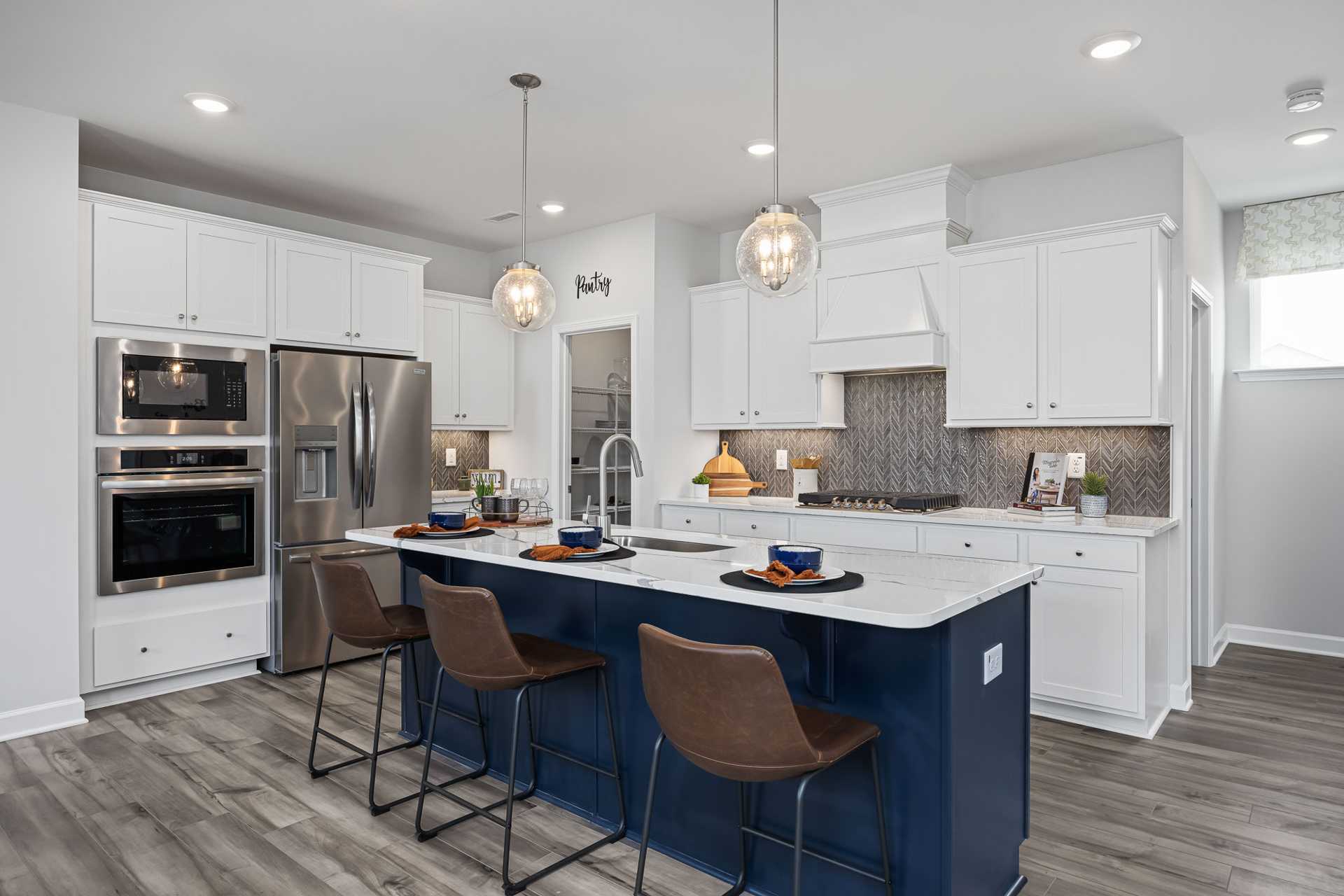 Modern kitchen at Beverly Place in Four Oaks NC featuring white shaker cabinets, navy island with leather stools, stainless appliances and subway tile backsplash