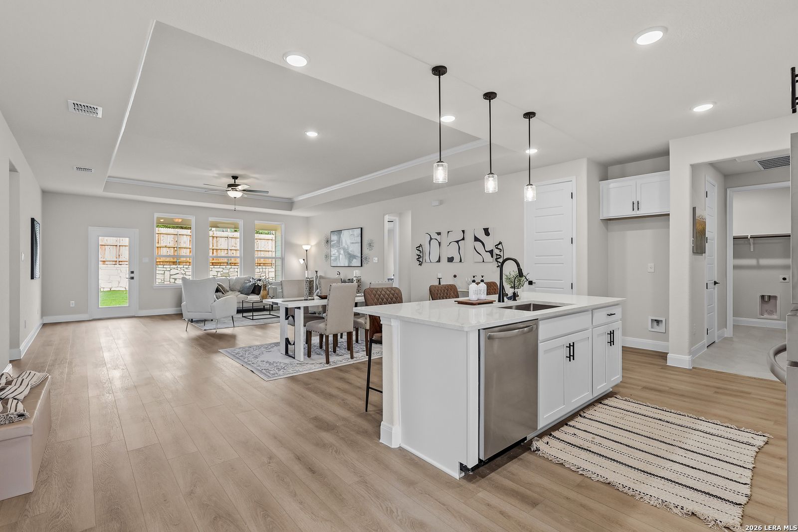 Open-concept living and kitchen with white island, stainless dishwasher, wooden floors, large windows in The Lanier G home, Castroville, TX