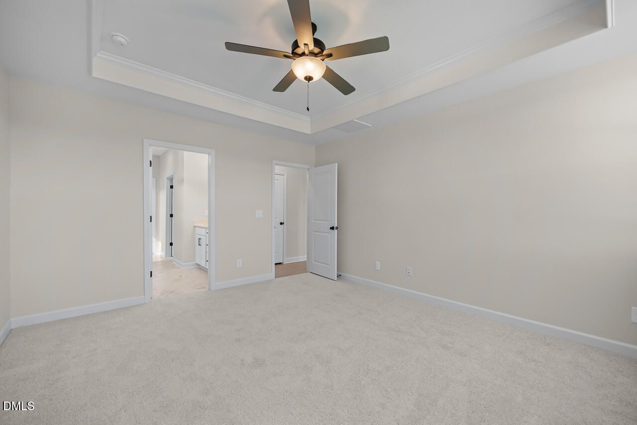 Spacious primary bedroom with tray ceiling, ceiling fan, and carpet in Davidson Homes The Ashport M plan, Wendell Ridge, NC
