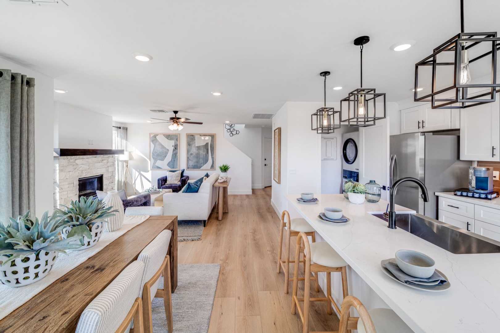 Open-concept kitchen and living room in The Wilmington with white cabinets, large island, stone fireplace, and hardwood floors